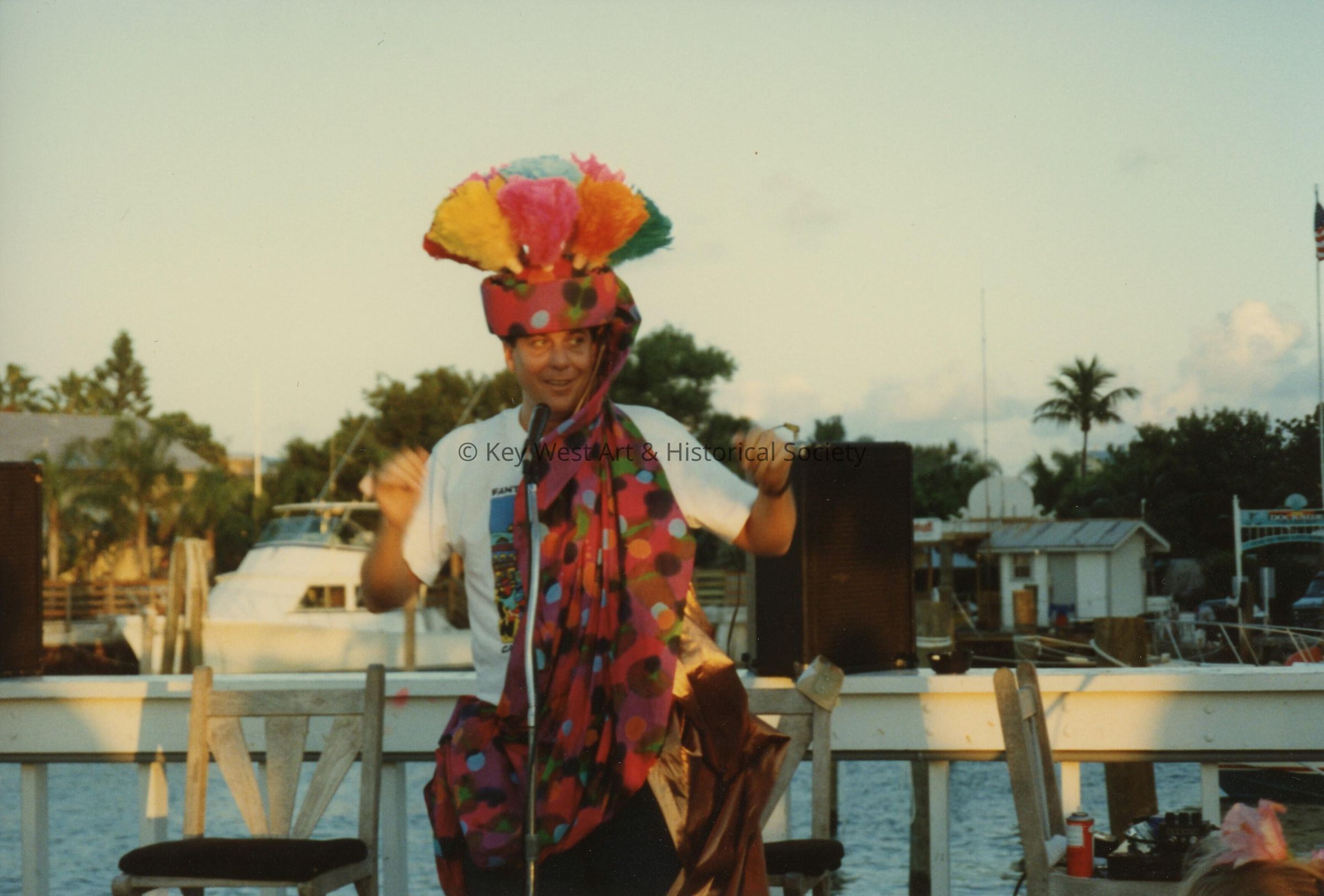 An unknown man dressed up talking into a microphone standing near the water