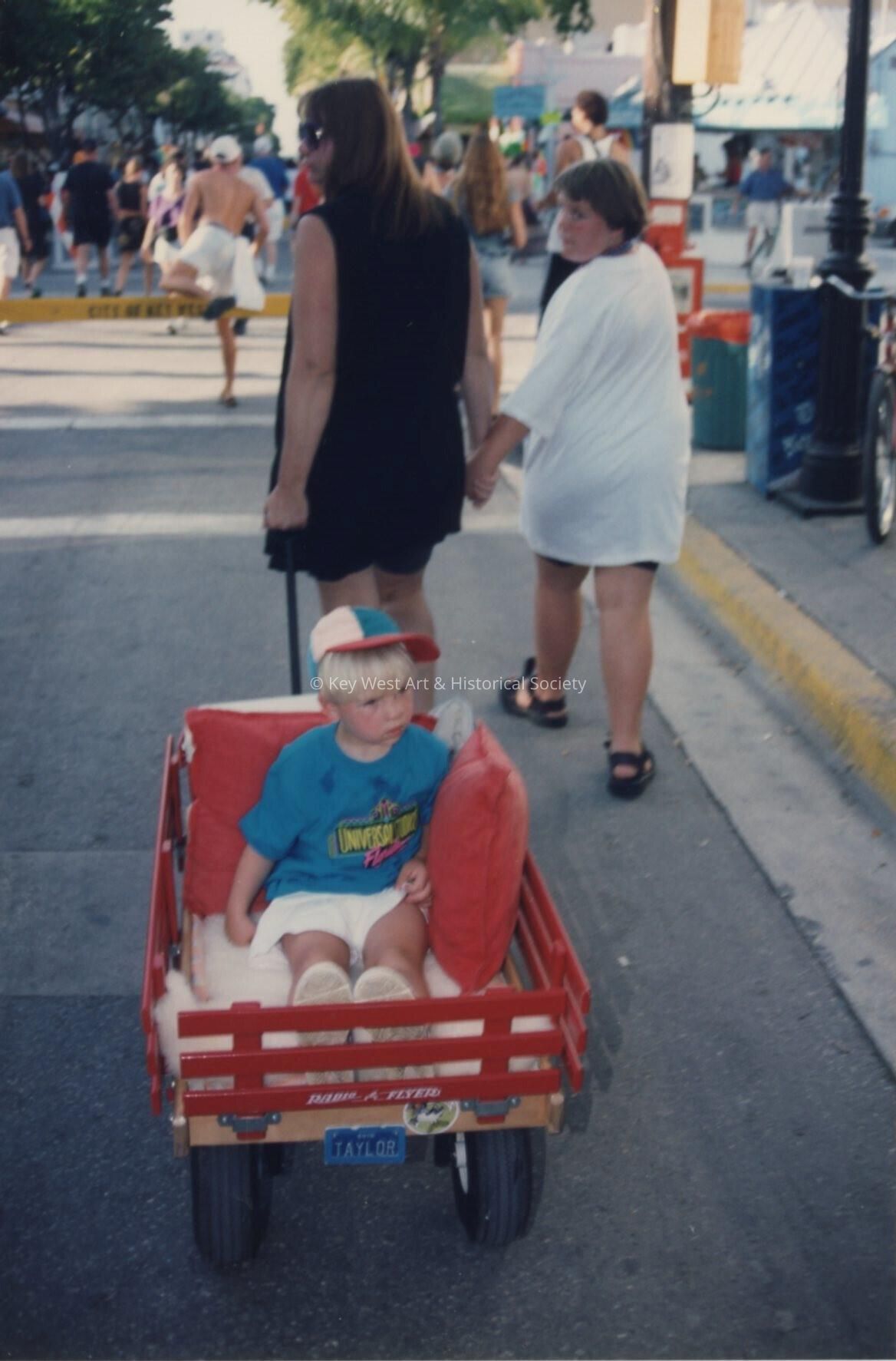An unknown woman walking with unknown kids, one is being pulled in a wagon.