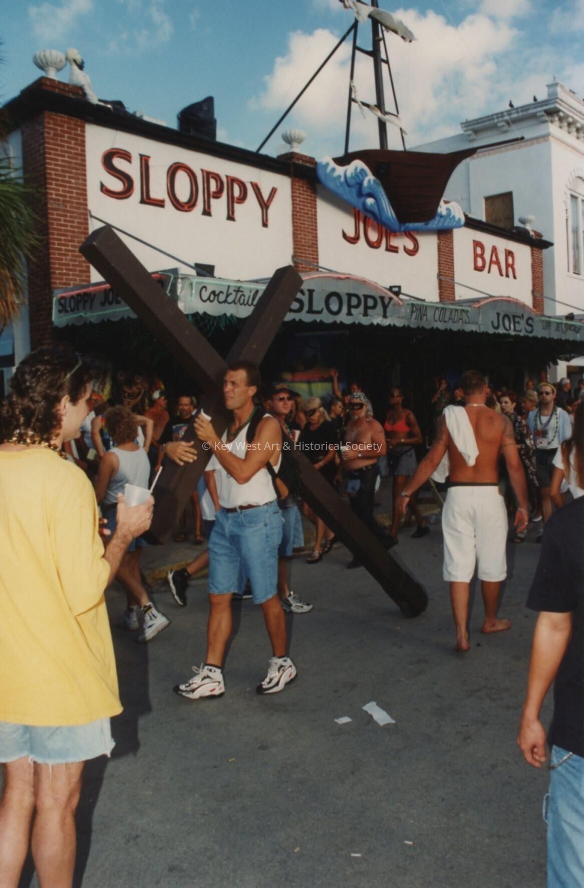 An unknown man carrying a wooden cross in front of Sloppy Joe's Bar.