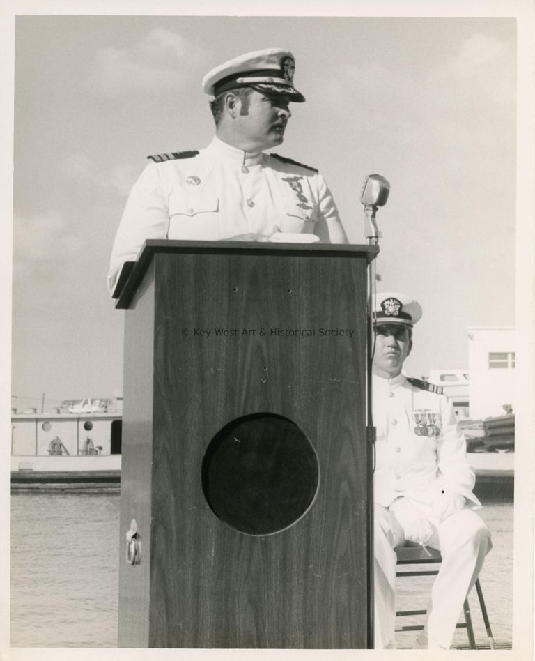 2 Men in uniform, one at the podium