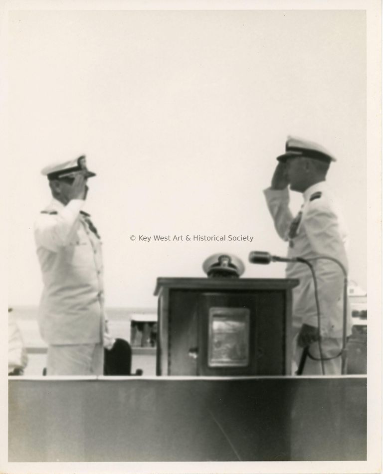 2 Men in uniform saluting each other near a podium