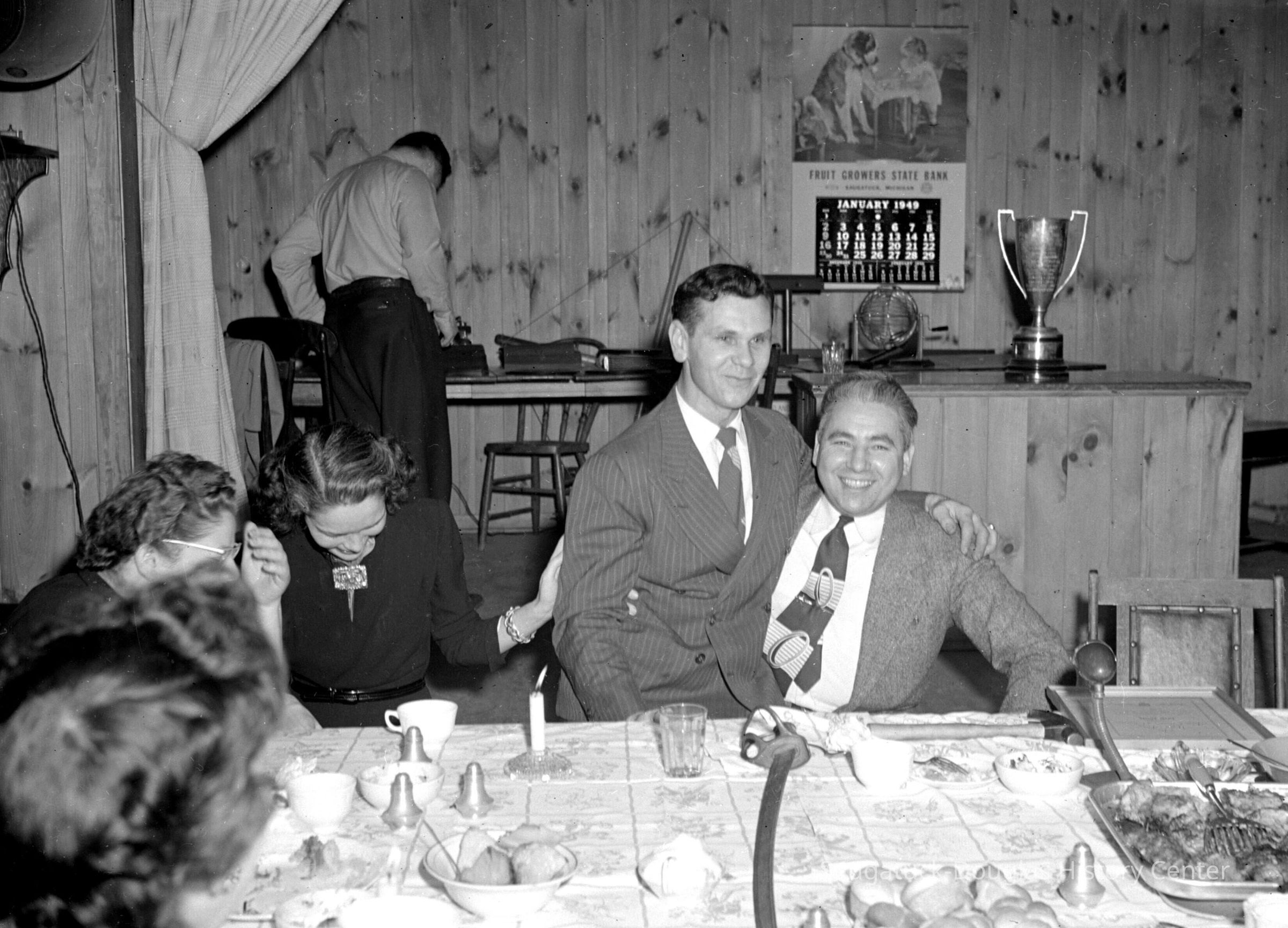 Jack Janis on the lap of Ev Thomas: From "Off the Record" — Jack Janis had just received the local "Distinguished Service Award" for 1949, presented by Thomas, charter president of the Junior Chamber of Commerce, at the American Legion Hall, on July 25, 1949. Mr. Janis was recognized for his volunteer work in organizing the village recreation program, which included the Oval Frolics, the Arts Week, the Venetian Night, the Village Christmas Party, Halloween night for kids, and so forth. Janis was the owner of the Twin Gables Hotel and had moved to Saugatuck in 1945.