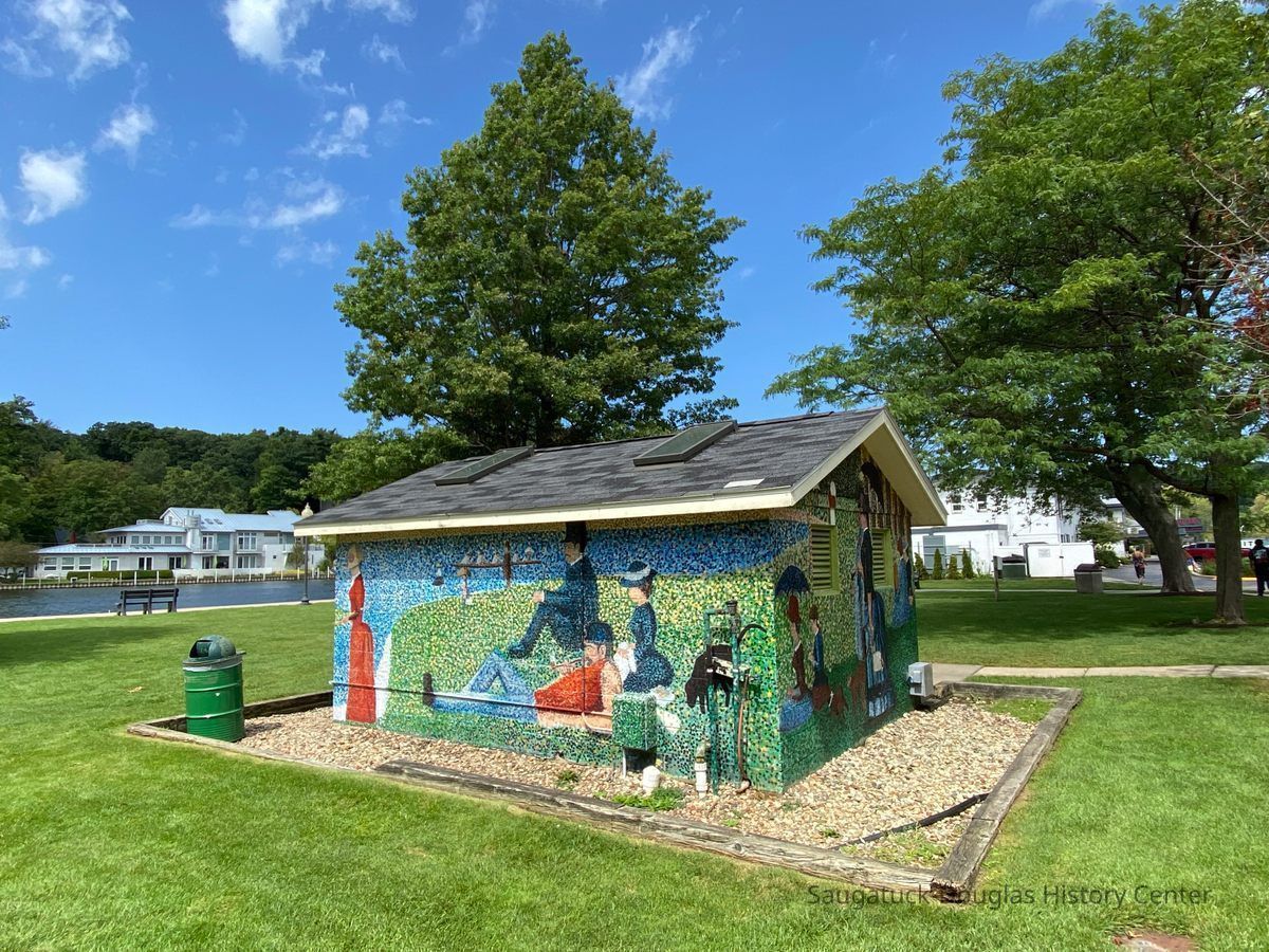 https://www.atlasobscura.com/places/seurat-at-saugatuck-s-restroom; In 1977, the head of the Wicks Park asked Carol Miron, who studied at the Art Institute in Chicago, to consider producing a “Saugatuck Seurat” on the walls of the restroom in the park. Saugatuck had just gained ownership of the park two years prior and wanted something memorable and artistic to reflect the creative character of its community.
Miron recreated “Sunday Afternoon on the lie de La Grande-Jatte” by Georges Seurat, accommodating the windows and doors seamlessly of the park’s bathroom.
When new restrooms were constructed down the street, the “Seurat” building was slated to be demolished. However, after objections from the surrounding community, the building was preserved. Subsequent artists, both professionals and aspiring high school students have continued to periodically refresh the eye-catching landmark. “Saugatuck’s Seurat” anchors the downtown park, inviting its viewers to imitate the leisurely activities of its weekenders by lounging on the lush grass.