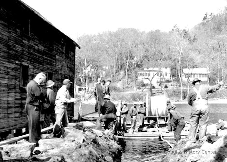          HM67LayingPipeRiver; This image was featured as History Mystery #65 with the solution: Village Public Works crew  laying new water pipe on the river bottom ca 1950.
   