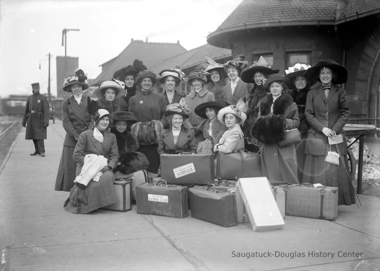          KColGaynorOrig.jpg 2.3MB; The Gaynor Club
These are the members of the then well-known K College women’s glee club. Extravagantly hatted and furred, they await a train that will carry them off for a weekend singing date. In the back row, the woman fourth from the left is faculty. Also in back, Florence Hartman with her ever-present pince-nez is just to the right of the girl with bird wings on her hat. The cop seems to be sans pistol but has a big stick and is keeping a sharp eye on things. Perhaps there was an ordinance against giggling. Even that seems unlikely with this well-behaved bunch.
George took this with his 5x7 view camera. He probably had to carry the big
camera case and tripod the half mile down hill from the college to the station. I wonder, did the girls help? From the direction of the eyes of some of his subjects, I’d guess he stood to the left of the camera with his rubber bulb and said or did something silly to get them all to smile. In the exact center of the back row stands a pretty girl with good cheekbones. Did she choose that spot — or did George?
Surprisingly, the Kalamazoo train station has hardly changed at all in the
ninety years that have passed.
   