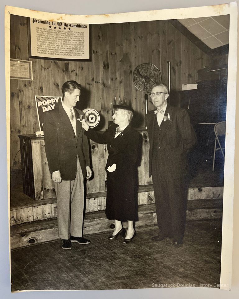          Memorial Day 1954; Lillian Morris pins poppy on lapel of Mr. Sholders[?] the president to Douglas village with Mr. George Wright, president to Saugatuck Village. Location: American Legion post 137 hall.
   