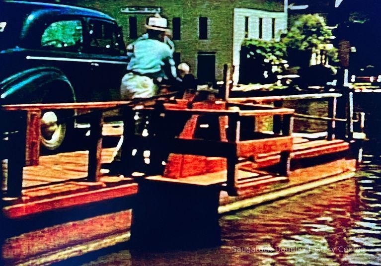          man cranking chain ferry to transport car across river
   