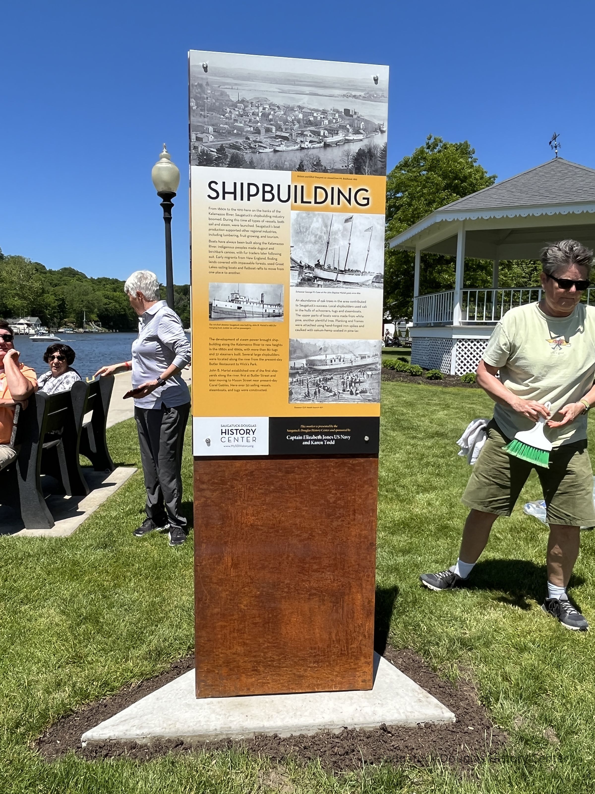 Installation of the interpertive panels on the steel makers, June 2, 2022; Julie Bizzis (gray shirt talking with people on bench) and Laura Peterson (with wisk broom)