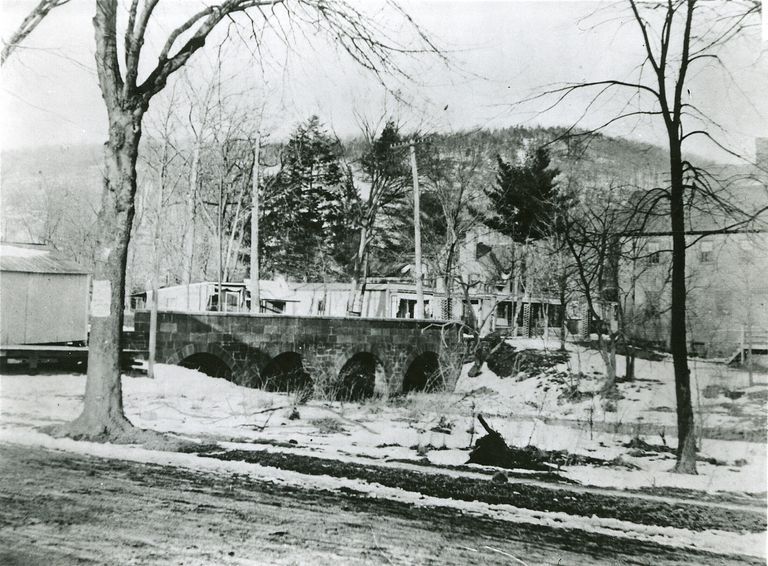          View is northward from Main Street. Visible from left: shed (then above bridge)-Percy Brown's Paper Store, Angelo Gentile candy store, notions, (after bridge) Vauxhall Inn (formerly Condits) and side of Lonergan's 