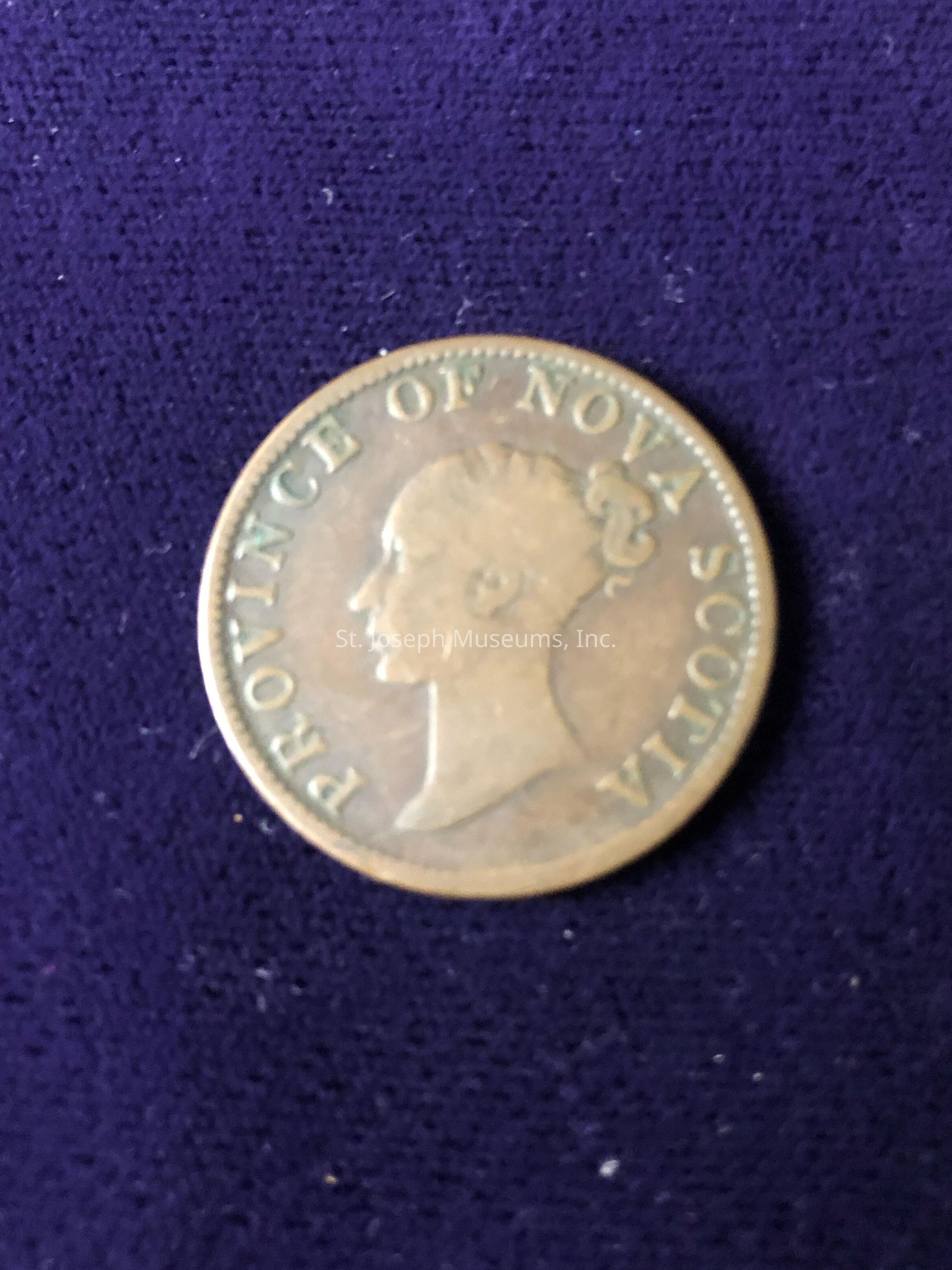 The coin bears an inscription that reads "PROVINCE OF NOVA SCOTIA" along the perimeter, surrounding a profile of a head in relief, facing to the left. The patina of the coin suggests age, and the surface has a slightly worn appearance, indicating it may have been in circulation for some time. The background contrasts with the coin, providing a dark, soft canvas that accentuates the coin's details. This coin is potentially historical, linked to the region of Nova Scotia, and reflects numismatic interest. The focus is sharp on the coin, illustrating its relief and inscriptions clearly, while the background remains plain, allowing full attention to be drawn to the coin and its engraved details.