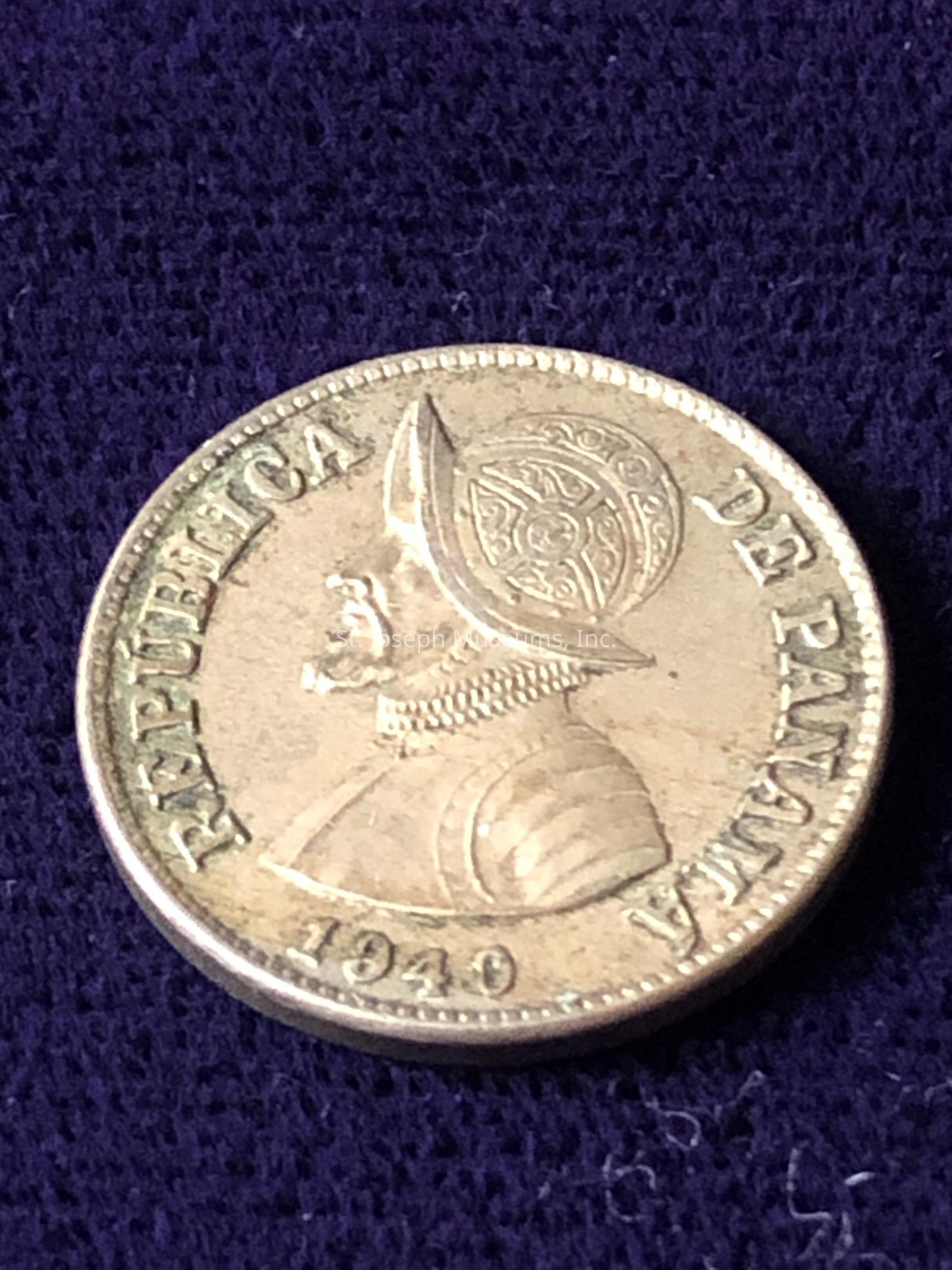 The image features a coin from the Republic of Panama, dated 1940. The coin showcases a detailed profile of a figure wearing a traditional conquistador helmet, which is ornately decorated. Surrounding the central image, the words "REPUBLICA DE PANAMA" are inscribed along the edge of the coin in a circular arrangement. The coin is metallic, likely made of a silver-toned material, and displays signs of age with slight tarnishing. The overall design is intricate, reflecting historical and cultural elements significant to Panama's heritage at the time.