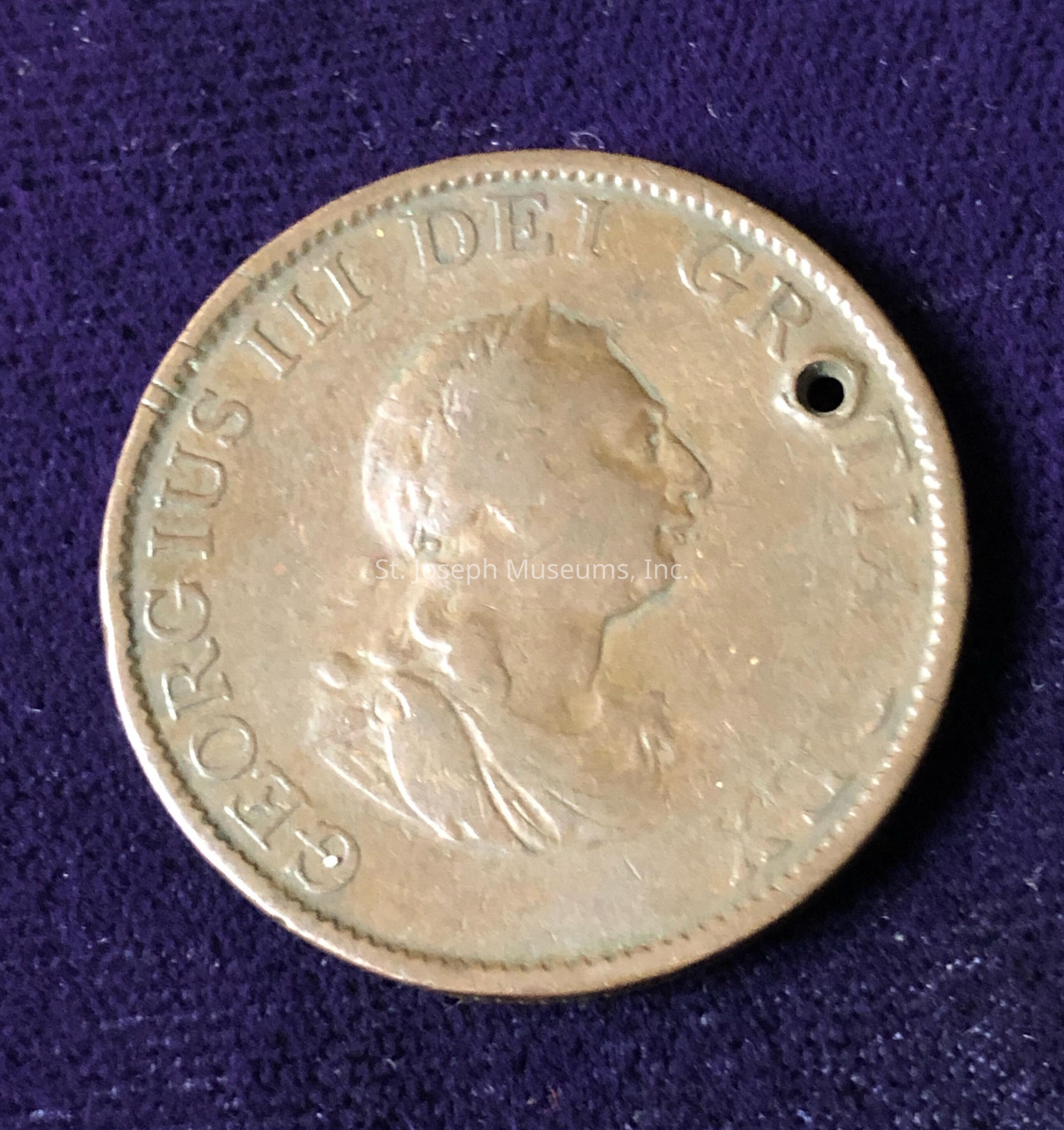 The image shows an old coin with the profile of a distinguished person facing right, surrounded by the inscription "GEORGIVS III DEI GRATIA" along the edge of the coin. The coin has a small hole near the top right, indicating it may have been worn as an ornament or pendant. The coin appears to be a historical artifact, possibly from the Georgian era, demonstrating signs of age and wear but still maintaining a clear depiction of its details.