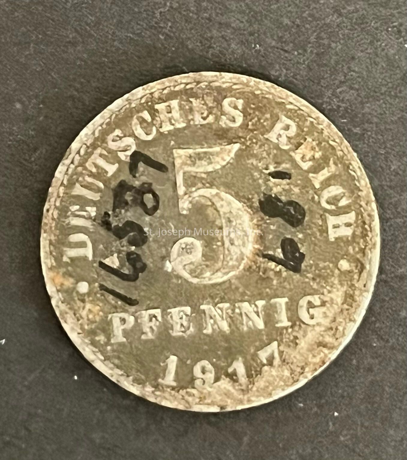 The image depicts an old, weathered coin from 1917 with inscriptions. The top edge features the words "DEUTSCHES REICH," indicating it belongs to the German Empire era. In the center, the number "5" is prominently displayed, signifying its denomination in pfennig, a former German currency unit. Below the numeral, the word "PFENNIG" is inscribed, confirming its value. Visible wear and tear suggest it has been in circulation.Despite its worn condition, the coin retains historical significance, offering insight into a past era's m onetary system. The coin sits on a neutral, dark background that contrasts with its metallic tones, highlighting its details. It serves as a tangible connection to the early 20th-century German state, reflecting the economic and cultural conditions of that time, while also being a possible item of interest for numismatists due to its age and historical value,