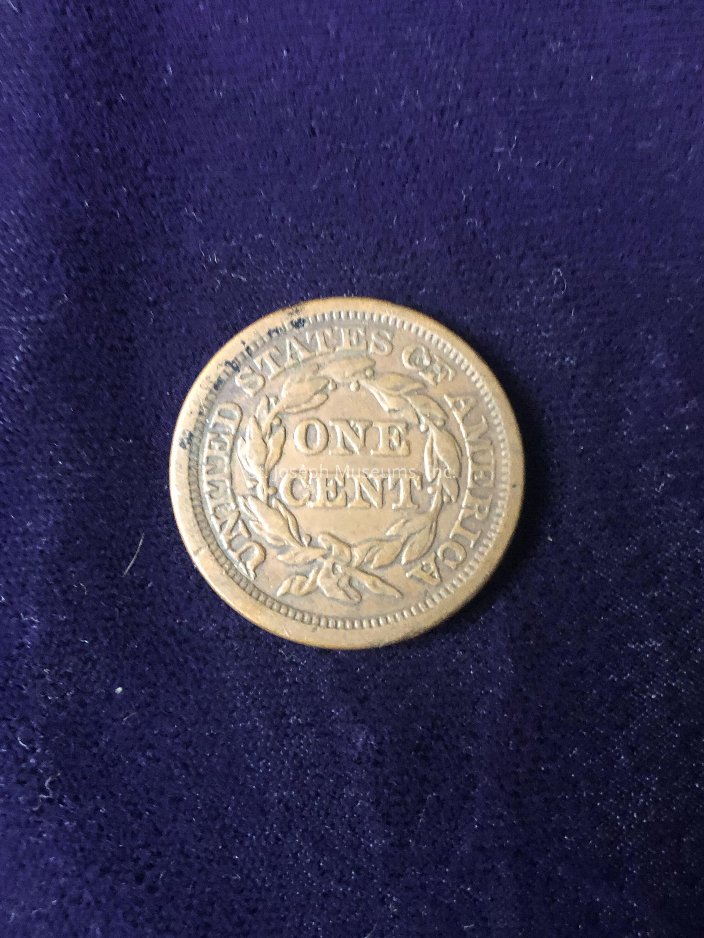 The coin features the inscription "UNITED STATES OF AMERICA" around the outer edge, with "ONE CENT" prominently displayed at the center, surrounded by a laurel wreath design. The patina and wear on the coin suggest age and historical significance, indicating it might be a collectible or of interest to numismatists. The detail in the engraving, especially the wreath, speaks to the craftsmanship of minting from a bygone era.
This image captures a piece of history encapsulated in a small, round, tangible form, connecting the present with the past through the very essence of currency that once circulated in the economy, representing not just monetary value, but also the cultural and historical context of its time.