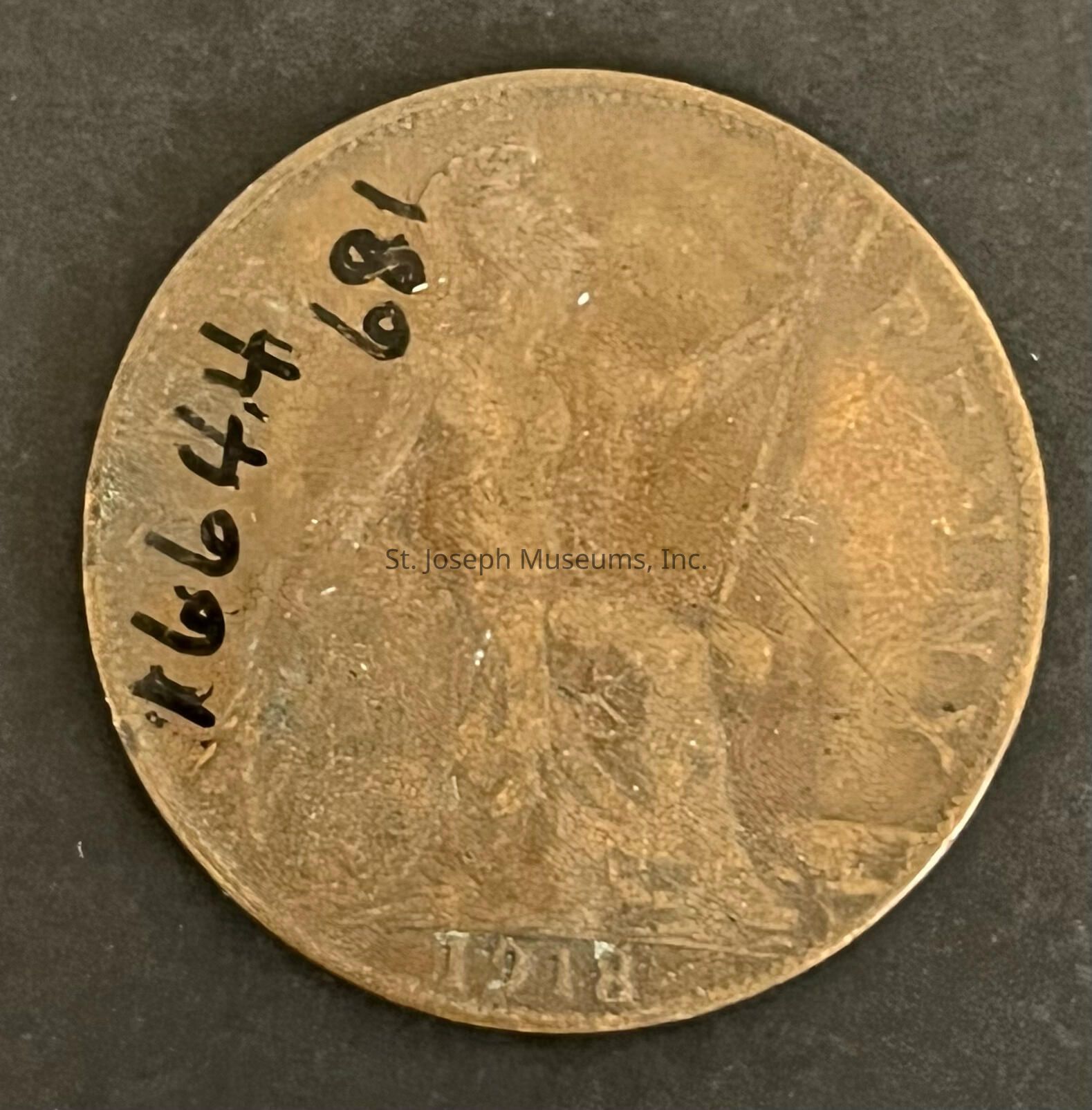 The image depicts an old, worn coin with a textured surface and visible signs of age, such as scratches and weathering. On the coin, there is an engraving of a seated figure holding a trident, which is faint but discernible. The numbers “1918” are etched near the bottom, indicating the year of minting. The coin's border is slightly raised and has a rough texture, contributing to its antique look. The overall color is a dull bronze, indicative of oxidation and age, and the design appears to be British.