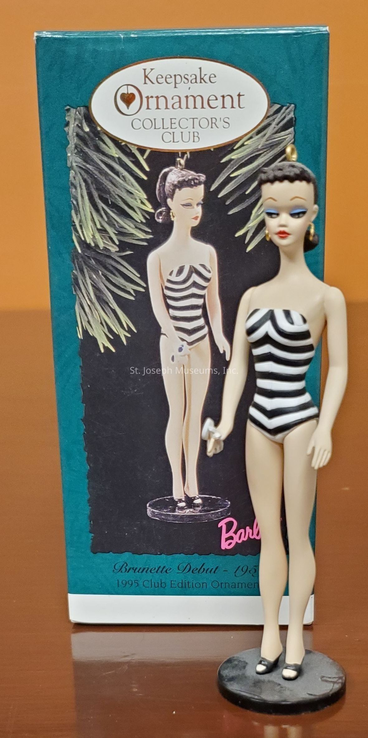 The image displays a collectible ornament featuring a vintage-style doll wearing a black and white striped swimsuit, reminiscent of a historic fashion doll design. This collectible is presented as part of the "Keepsake Ornament Collector's Club," with packaging describing it as the "Brunette Debut - 1959" and labeled "1995 Club Edition Ornament." The box shows a picture of the ornament against a backdrop of pine branches, suggesting a Christmas or holiday theme for the collectible. The doll itself stands on a black circular base, highlighting its decorative nature and the attention to detail in its design.