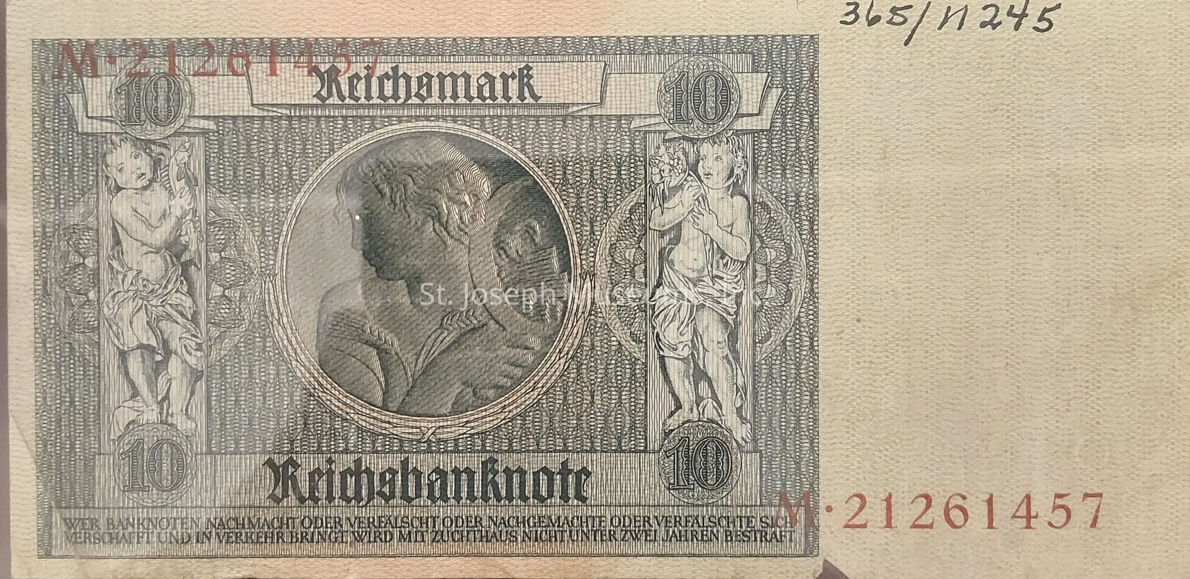 The image displays a vintage German banknote with "Reichsbanknote" prominently printed at the bottom, indicating its value of 10 Reichsmark. It features intricate designs, with two cherubic figures flanking a central medallion that portrays the profile of a classical figure. The designated value "10" appears within ornamental circles in the top corners, and serial numbers are printed in bold red on both the top and bottom edges of the note. The background pattern features a detailed, woven texture, while a fine-print warning in German against counterfeiting is located at the bottom. The bill combines artistic and historical elements.