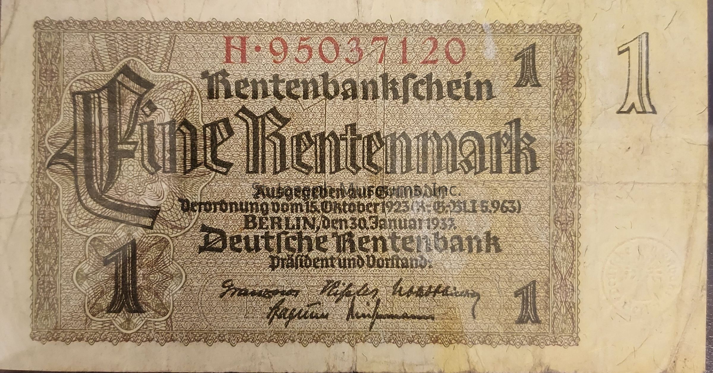 The image displays a historical German banknote called a "Rentenbanknote," specifically valued at "Eine Rentenmark," with intricate vintage design elements such as decorative borders and ornate script. The prominent large text includes denominations of "1" at each corner, with an elaborate gothic style for the word "Eine Rentenmark," which spans the center. The note is marked with a serial number "H-95037120" in red at the top. Below the main text, there is additional information in smaller font detailing the issuance, which mentions "Berlin, den 30. Januar 1923." This text likely outlines the legal and financial context of the currency issued by the Deutsche Rentenbank, with signatures included at the bottom, possibly representing financial officials or bank authorities. The overall condition shows signs of age, and the paper color suggests it is slightly yellowed and worn, indicating historical significance, likely from the Weimar Republic era in Germany.