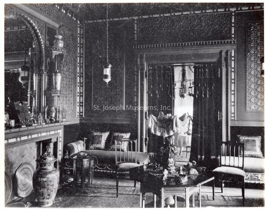 Tootle Mansion, Moorish Room, c. 1900: Copyright: 84.21.2029 Tootle Mansion, Moorish Room, c. 1900
The Tootle Mansion Moorish Room, captured in a black and white photograph from around 1890, displays its rich, ornate design with elaborately detailed paneling and upholstered settees flanking the doorway to the next room, while a north wall fireplace is adorned with decorative vases and intricate architectural elements; a central table stands prominently with two chairs, surrounded by various artful decorations, which reflect the sophisticated taste of the Tootle family during its occupancy, expertly restored by Portier & Stymus of New York.