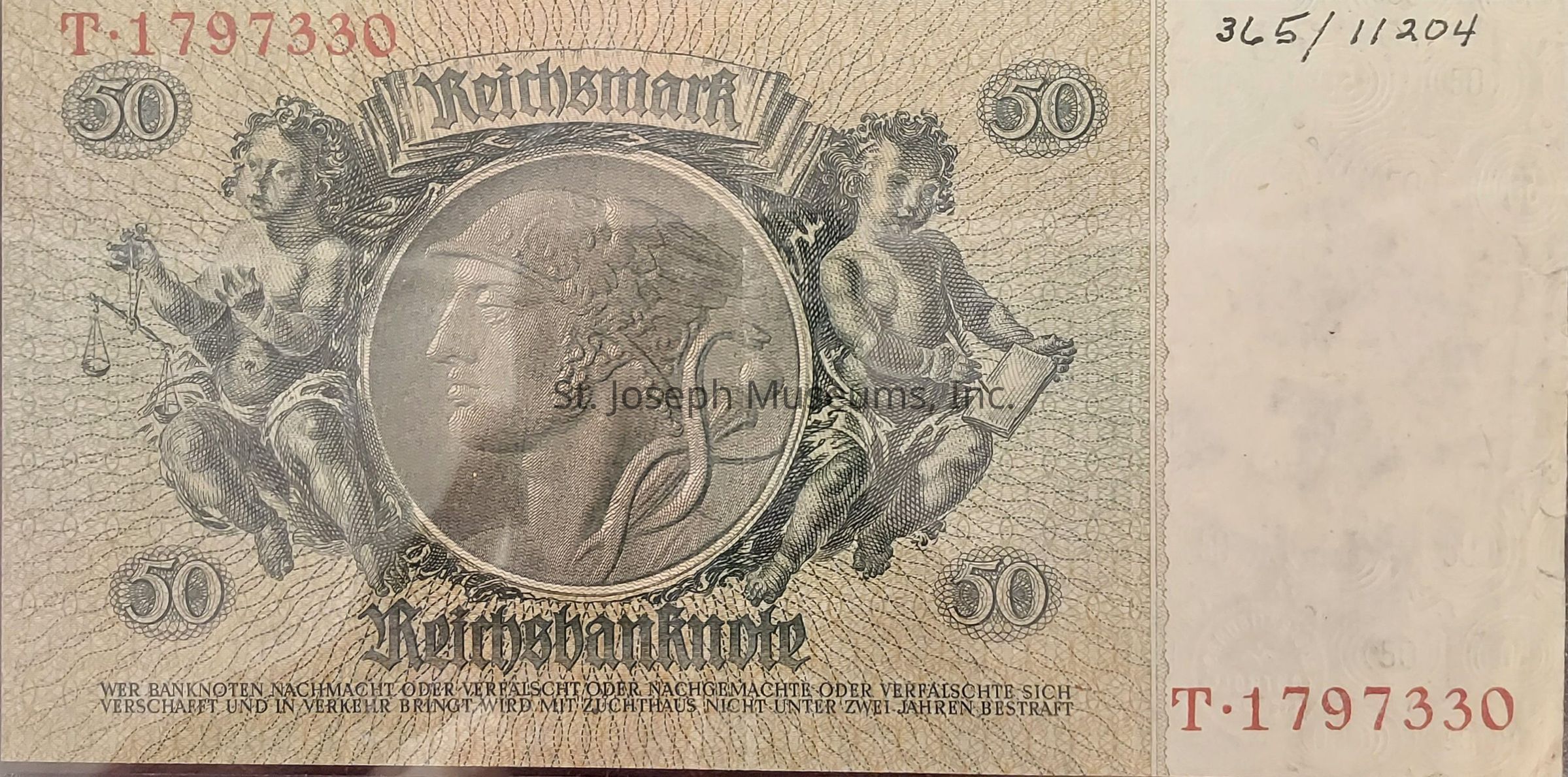 The image depicts a historical 50 Reichsmark banknote, featuring intricate designs and artwork. At the center, there is a large circular emblem with a classical profile of a helmeted figure, reminiscent of ancient Roman or Greek art. This central image is flanked by two cherubic figures; the one on the left holds scales, symbolizing justice, while the one on the right appears to be writing in a book. The word "Reichsmark" is prominently displayed above the central emblem in Gothic script, and "Reichsbanknote" is written below. The number "50" is repeated in ornate medallions in each corner. A serial number, "T. 1797330", is printed in red ink in the upper left and lower right corners. A warning text, in German, is printed at the bottom, cautioning against counterfeiting.