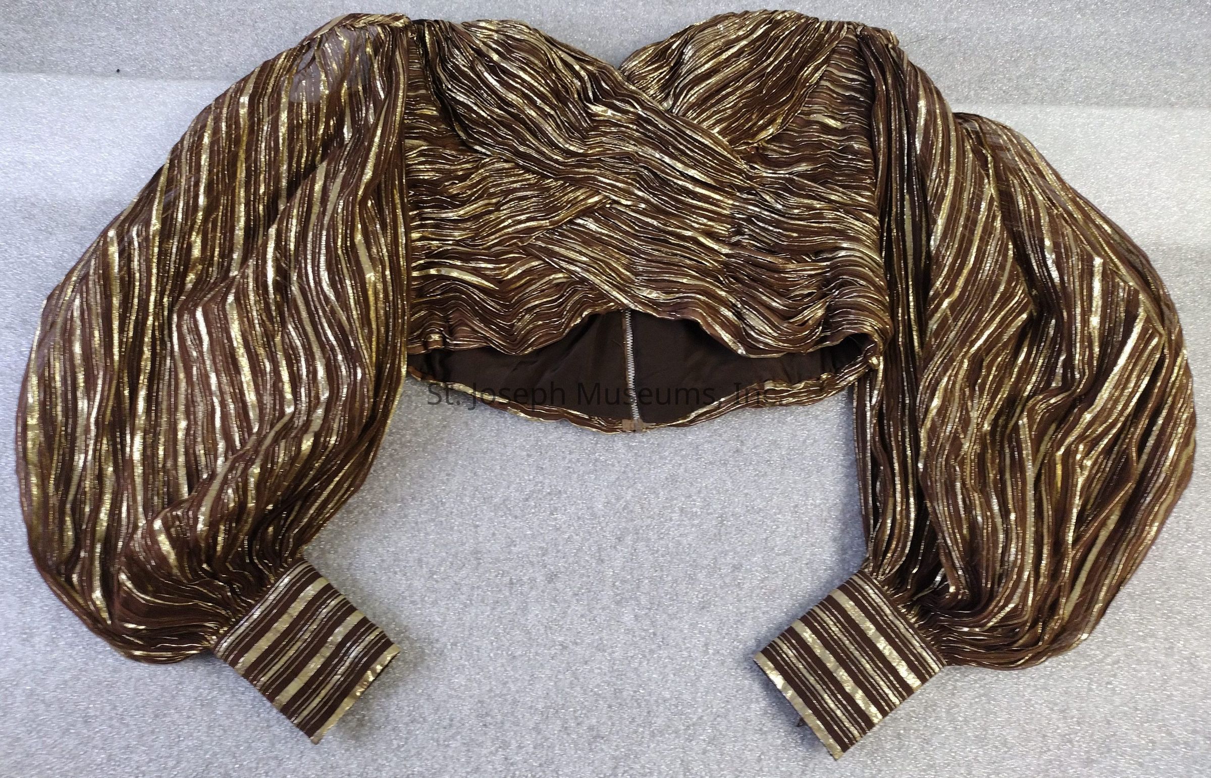The image displays a structured bodice measuring 12 inches in length, crafted from a blend of nylon and mylar. This garment is characterized by its textured brown and gold striped pattern, with long sleeves that include zipper closures at the cuffs. The back of the shirt is fastened using a zipper closure.