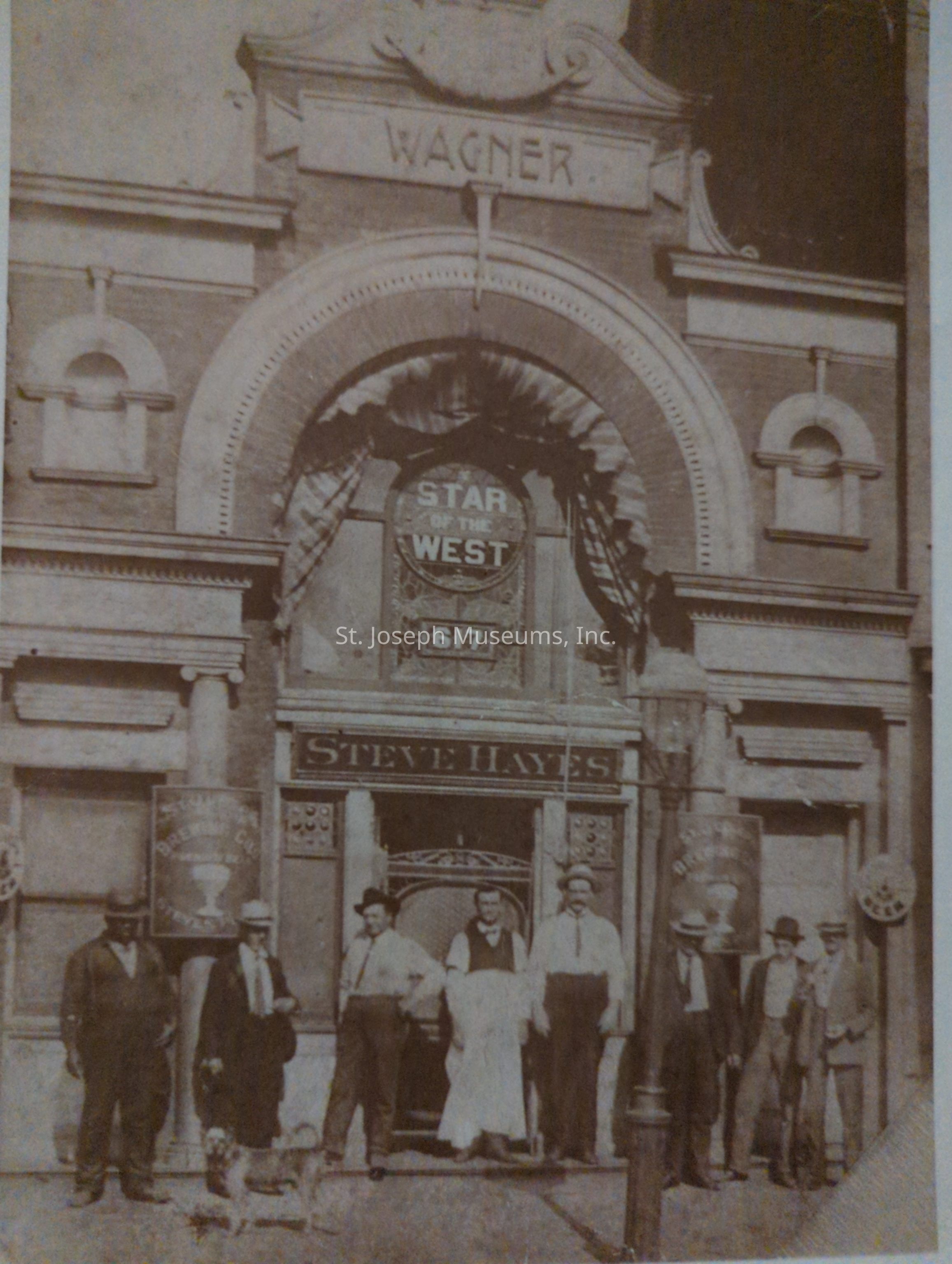 Black-and-white photo of a group of men standing in front of Steve Hayes's Saloon at 617 South 8th Street, dressed in period clothing. The saloon features prominent signage, including "Star of the West," and showcases ornate architectural details. The men appear relaxed, possibly employees or patrons.