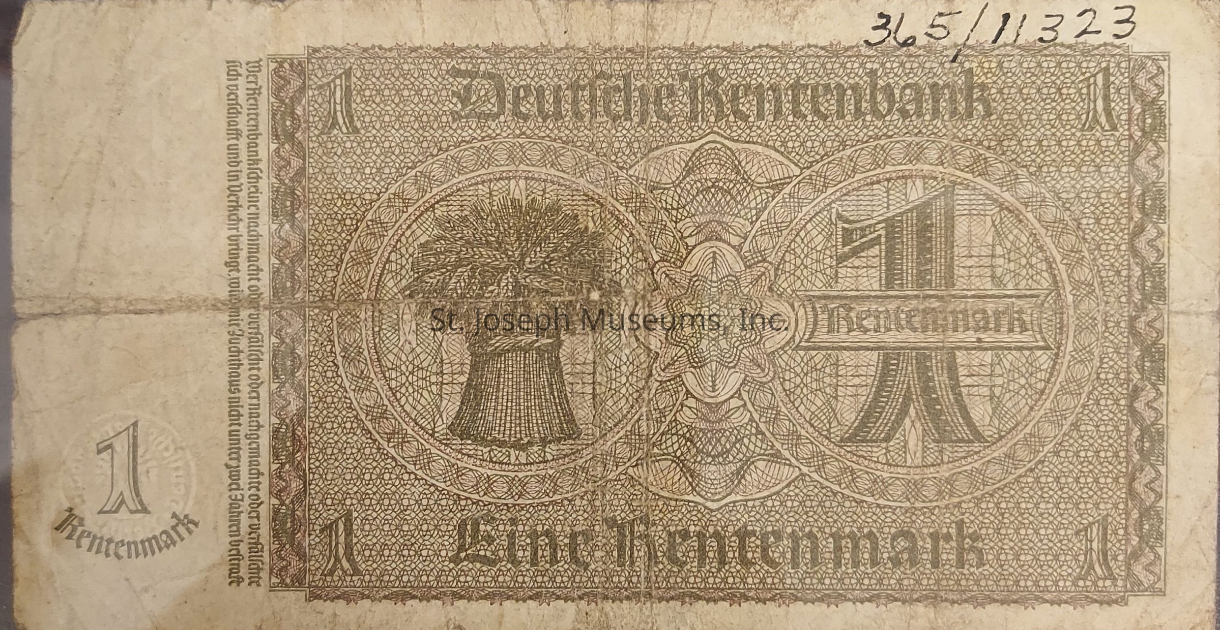 The image displays an old German currency note, specifically a 1 Rentenmark bill, from the time when the Deutsche Rentenbank issued such notes. The design is intricate, featuring a central motif with the number "1" prominently displayed in a decorative, geometric pattern, interlaced with German script. On the left side, there is an artistic depiction of a sheaf of grain, symbolizing agriculture and economic stability. The bill is worn and shows visible creases, indicating its age and usage. At the top right, handwritten numbers suggest a serial number or possibly an identification mark. The borders are elaborately designed, framing the text and imagery, which are rendered in shades of brown, adding to its vintage aesthetic.