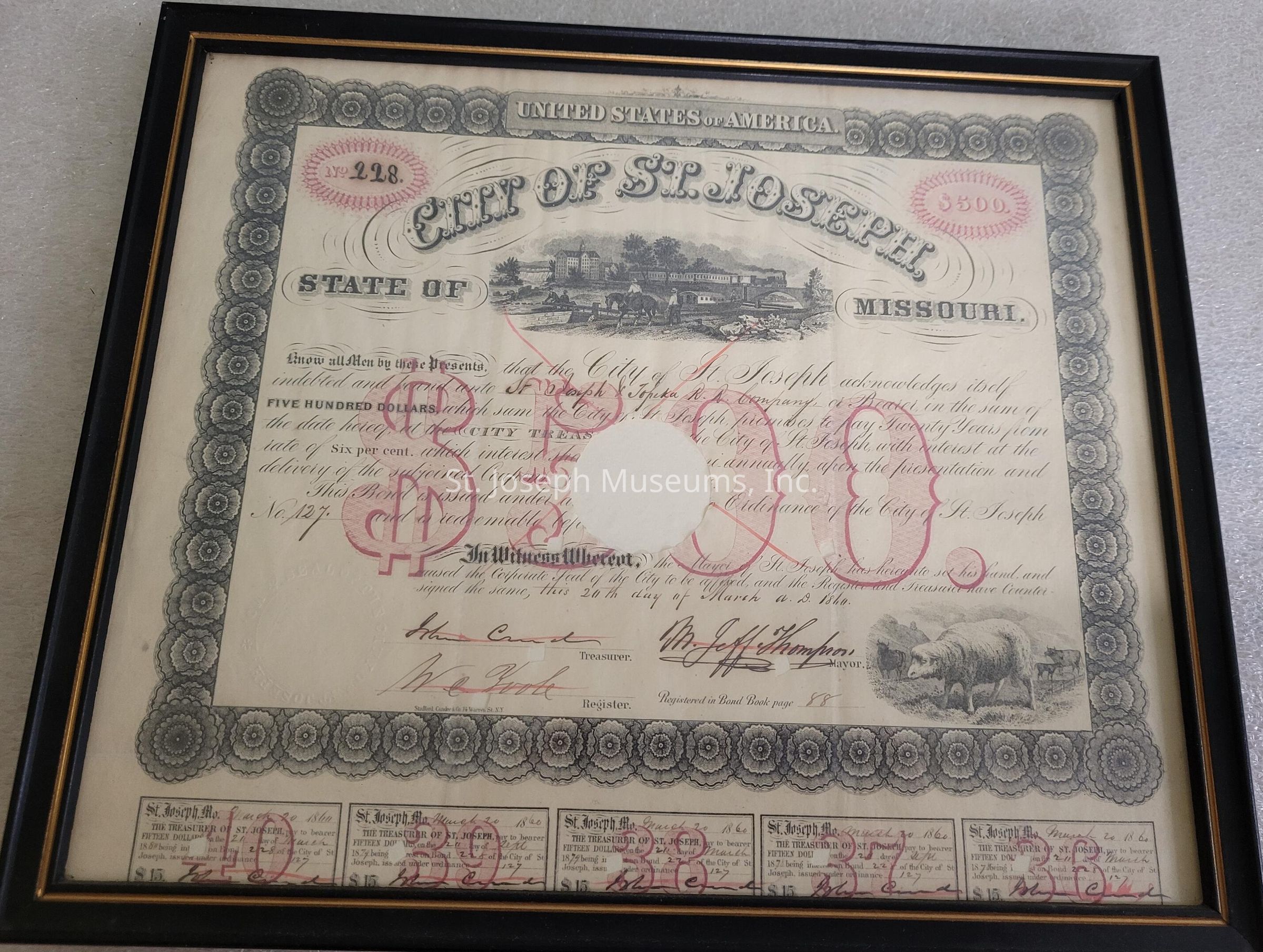 The image shows an ornately designed, framed document from the "City of St. Joseph" in the "State of Missouri," featuring intricate detailing around the border. The document is titled "UNITED STATES OF AMERICA" and appears to be a financial certificate or bond, with the prominent amount of "$500" displayed in large red lettering. It includes sections for signatures labeled "Treasurer" and "Register" at the bottom. The center of the certificate has a blank, circular area, possibly indicating cancellation. A small illustration of a building is at the top, while an artwork of a cow is at the bottom right. There are several coupons at the bottom, showing numbers and text related to payment or interest collection. The document has an antique appearance, reflecting its historical significance.