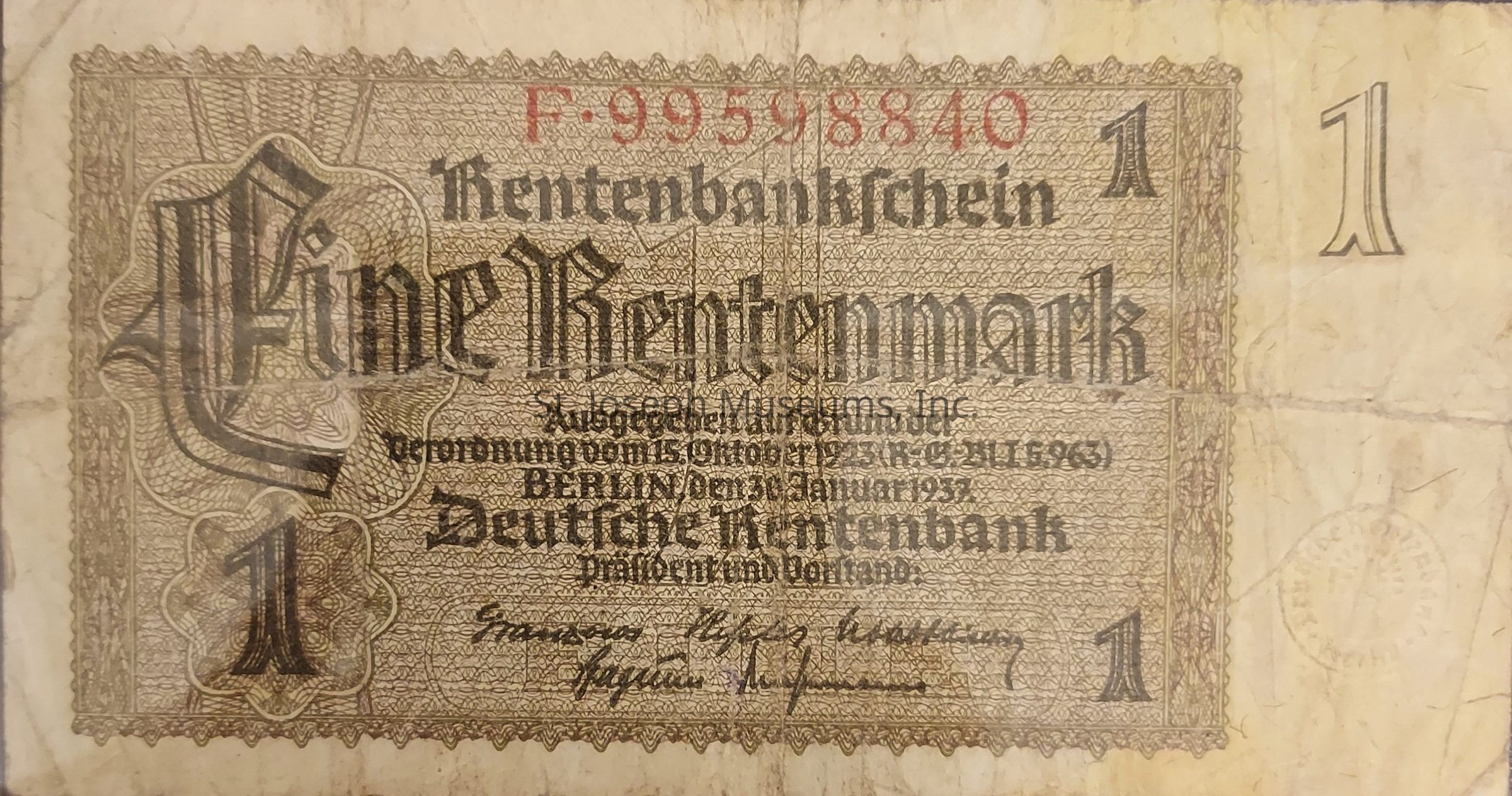The image displays an old German banknote, specifically a "Rentenbankschein" worth one Rentenmark, which was a currency issued in post-World War I Germany. This note prominently features the words "Eine Rentenmark" in large, ornate type, surrounded by intricate patterns and designs that frame the central text. The number "1" is positioned in the corners, indicating the denomination. There is a serial number printed in red at the top, while additional German text, possibly detailing the issuing authority and legal information, is printed below. The wear and age of the note are evident, with visible creases and a somewhat faded appearance.