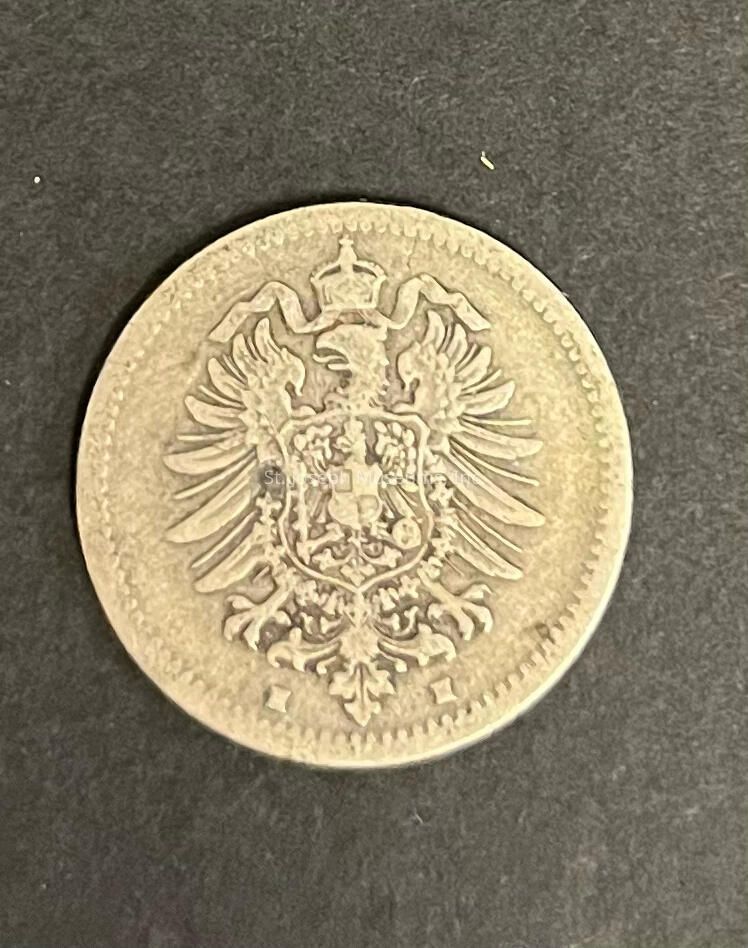 The image showcases an intricately designed coin against a dark background, featuring a centrally placed heraldic emblem engraved with a double-headed eagle, wings spread wide and crowned at the top, encircled by a precise border design. This emblem is reminiscent of old European heraldry, suggesting that the coin may have historical significance or origins, possibly from a European region with ties to such symbols. The detailing on the eagle and crest is finely crafted, indicative of a minting process that involved careful attention to detail, common in coins of significant age or ceremonial importance. The coin’s surface appears slightly worn, hinting at its age and possible circulation history, or it may have been kept as a collector’s item, preserved for its historical or monetary value. The tactile texture and patina suggest authenticity and possibly a mixture of metals traditionally used in ancient coinage. As a piece, it evokes a sense of curiosity about the era and culture it represents, offering a glimpse into the artistic and functional aspects of currency from