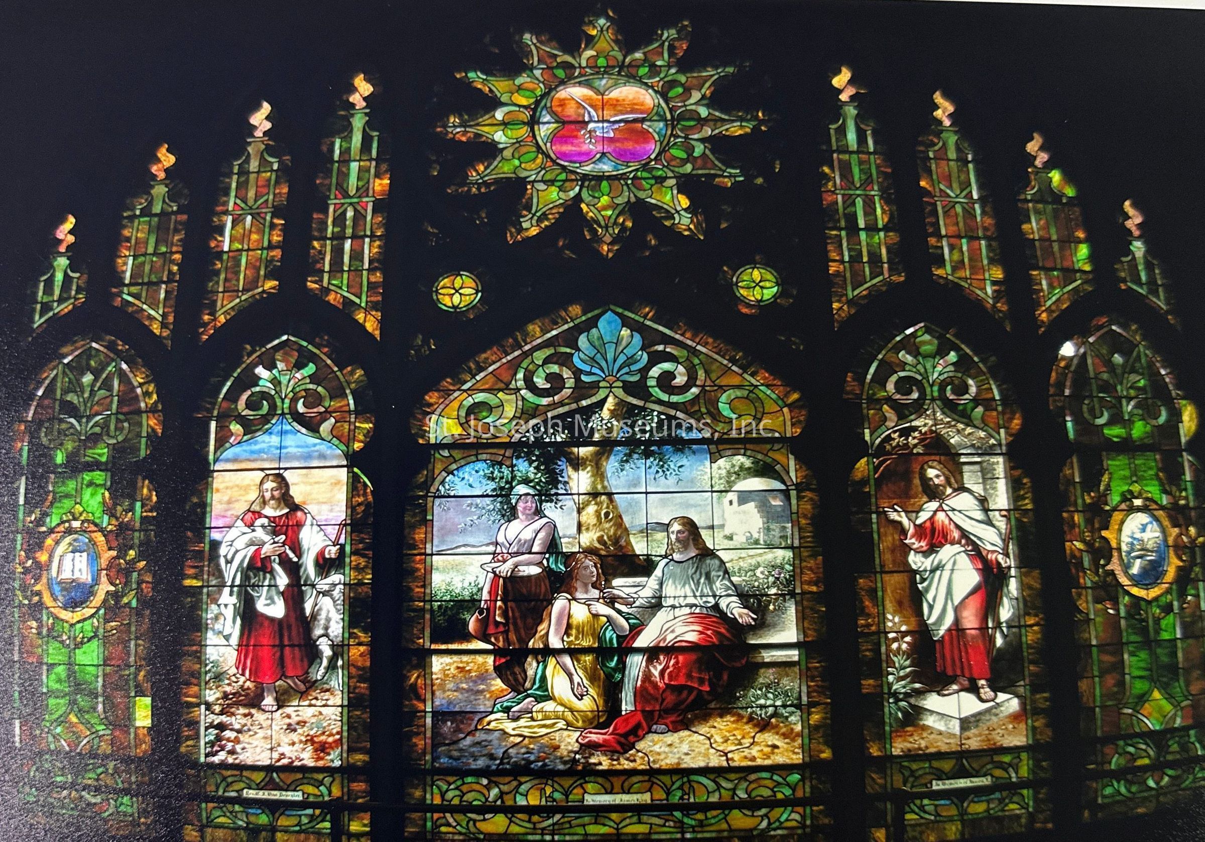 Interior colorized photo of stained glass window at Francis Street First United Methodist Church. There are 5 large arched panels along the bottom, the first on the left and the last on the right have geometric patterning and laurel framed portraits of religious iconography. The middle three panels depict a religious scene with decorative vine framing on the edges. Above the middle most panel is a circular sunburst shaped frame with a peace dove in the middle, with two triangular frames with small circular windows with four point patterns in each, connecting the sunburst and the middle arch. On either side are 4 tall windows with torch iconography and 4 smaller connecting panels above to make the large arched window.