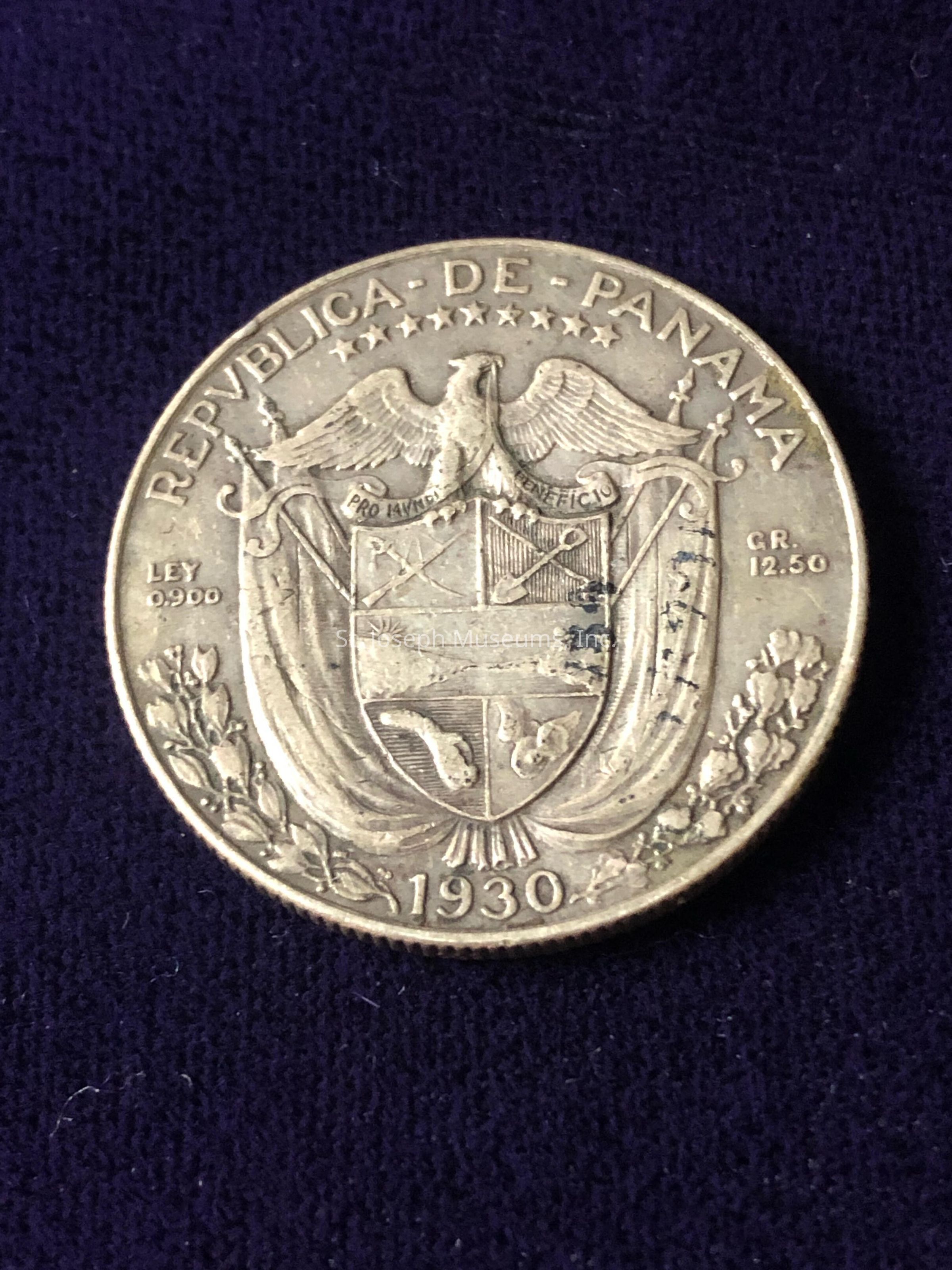 The image depicts a 1930 coin from the Republica de Panama. The coin features intricate detailing, including a heraldic shield topped by an eagle with outspread wings, which is typical of national emblems signifying strength and sovereignty. Surrounding the eagle are nine stars, likely representing the nation's provinces at the time. The text "REPUBLICA DE PANAMA" is inscribed around the upper edge of the coin, indicating its origin. Additionally, the text "LEY 0.900" and "GR 12.50" are also visible, providing information about the coin's composition and weight. Beneath the shield, the year "1930" is prominently displayed, denoting the minting year, which gives historical context to the coin. The intricate artwork and historical inscriptions hint at the coin's cultural and num