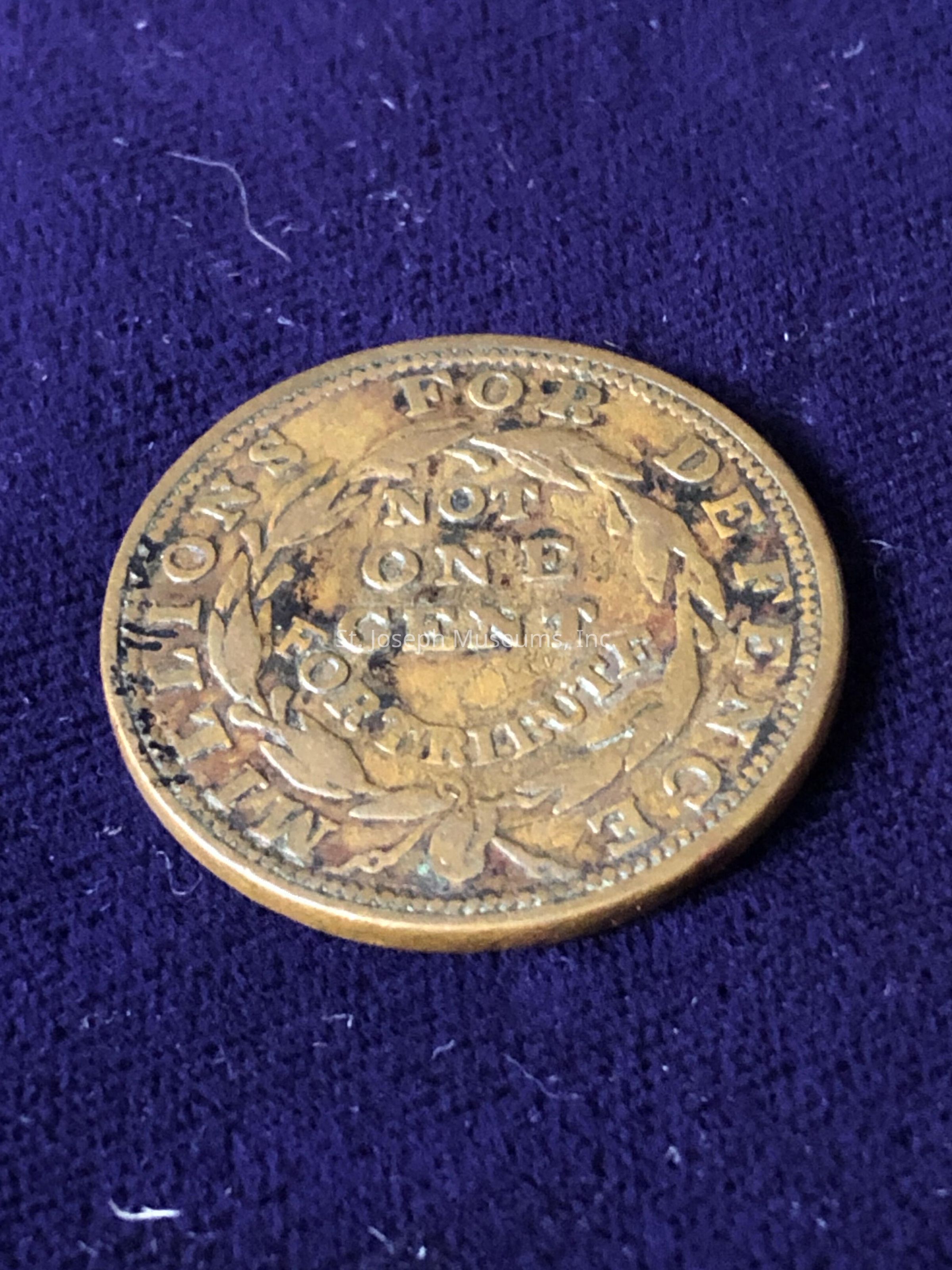 Text that reads "NOT ONE CENT FOR TRIBUTE," surrounded by decorative elements including a wreath, and possibly used as a political or protest piece in its time, showcasing its aged and weathered brass appearance with signs of wear around its edges, suggesting its antiquity and historical significance, possibly from the era of economic or political statements where such tokens were used for making strong messages or stances against policies, thus reflecting a piece of historical rhetoric in numismatic form, and capturing an era's sentiment in metal, symbolizing an expression not intended as currency but rather a statement.