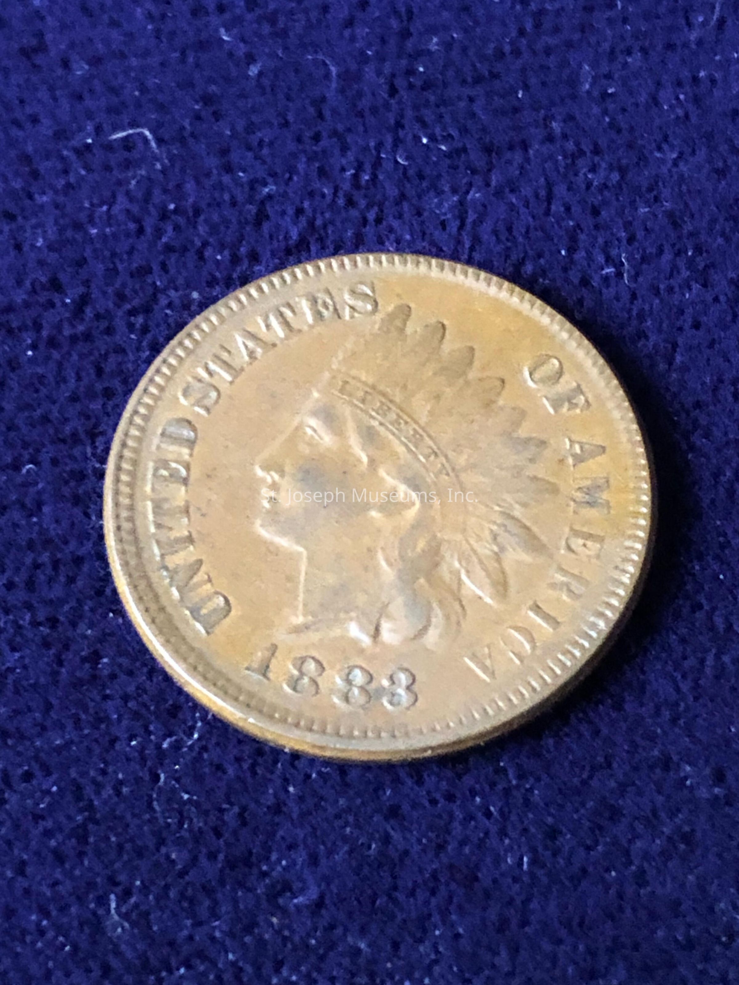 The image depicts an 1883 Indian Head cent, which is a historical coin from the United States. The coin features the profile of Liberty wearing a Native American headdress on the obverse side, and the words "UNITED STATES OF AMERICA" encircle the portrait. Below the bust is the year of minting, "1883." The coin is made of bronze and has a distinct copper-like appearance, giving it a warm, reddish hue.The coin is a collector's item and represents a significant period in American numismatic history, being part of the series minted from 1859 to 1909. Its design reflects the era's artistic and cultural elements, combining American iconography with an emblematic representation of Liberty.