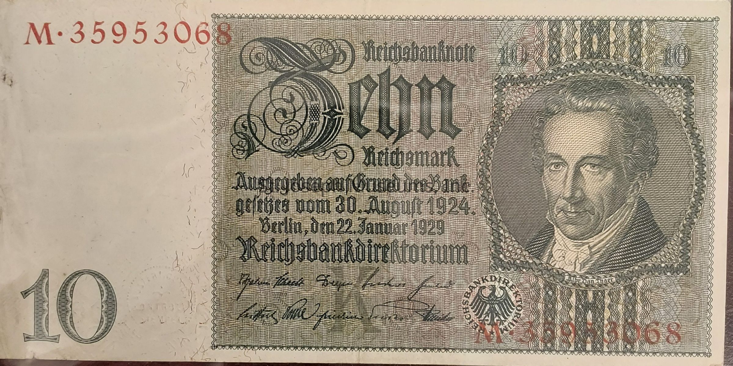 The image displays a historic German banknote, specifically a 10 Reichsmark note, dating from the Weimar Republic era. On the right side, there is an intricately detailed portrait of a man with distinct facial features, enclosed within an ornate oval border. The left side prominently features the word “Zehn” in decorative Gothic script, indicating the denomination. Below the denomination, inscriptions in German provide details about the issuance, including the date "22 Januar 1929" and legal references. The top left corner shows the red serial number "M 35953068." Ornamental patterns frame the entire note, reflecting the artistic style of the period.