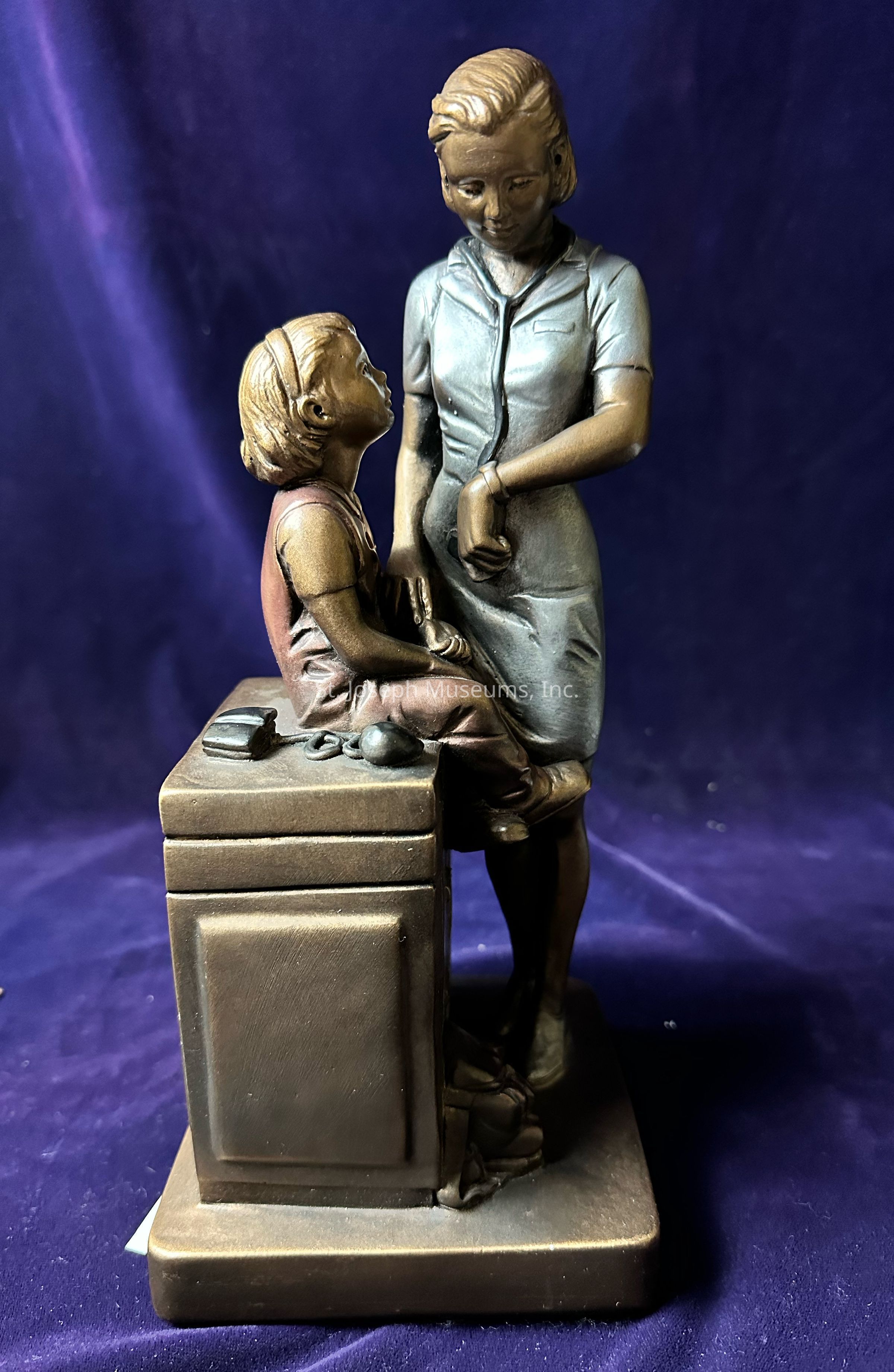 The image depicts a bronze sculpture of a woman and a girl in a seemingly tender and heartfelt moment. The woman is standing, slightly leaning forward and looking down, engaging with the girl, who is sitting on a block-like structure with her head tilted upward, as though listening intently or speaking. The woman's attire gives her a poised appearance, and her arm is gently resting on her waist, adding an element of casual sincerity to the scene. The girl, with her hair pulled back, appears to be seated comfortably, possibly conveying a moment of trust or shared understanding between them. This interaction creates an aura of warmth and connection, highlighted further by the fine details of their expressions and posture, bringing the scene to life against the deep, rich backdrop. The sculpture beautifully captures the emotional essence of the relationship shared, evoking feelings of nostalgia and familial warmth.