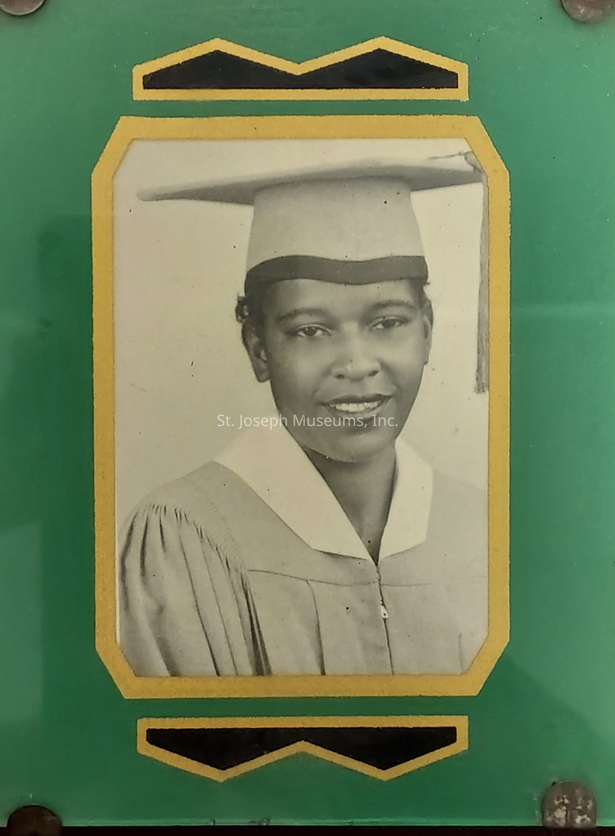 The image shows a black and white portrait of a smiling individual wearing a graduation cap and gown, suggesting the moment is a graduation ceremony; the photograph is bordered with a yellow frame that contrasts against a green background, giving the overall presentation a formal yet celebratory appearance.