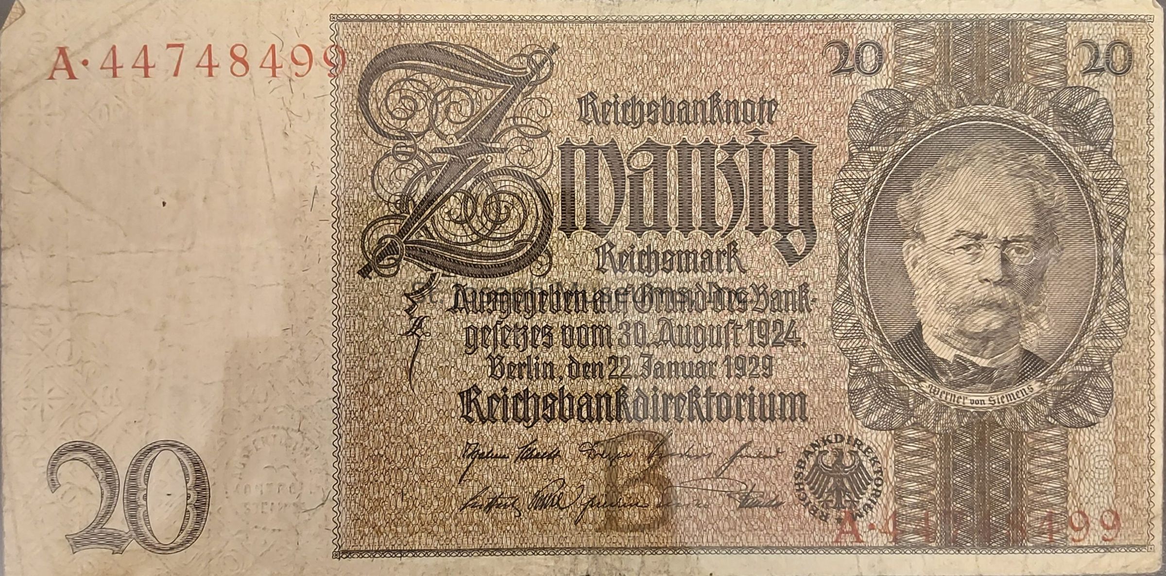 The image shows an old German banknote with a denomination of 20 Reichsmark, prominently displaying intricate designs and text. On the left side, a large, ornate number 20 is visible, while the right side features a detailed portrait of a distinguished man with glasses and facial hair, encased in an oval frame. The central part of the note is decorated with elaborate calligraphy and text that references the Reichsbank and the issuance date. The serial number is printed in red at the top left and bottom right corners, adding a striking contrast to the predominantly brown and beige hues of the note. There are signatures and a seal near the bottom, suggesting authenticity and authority. The complex patterns and textures throughout the banknote add to its historical and aesthetic interest.