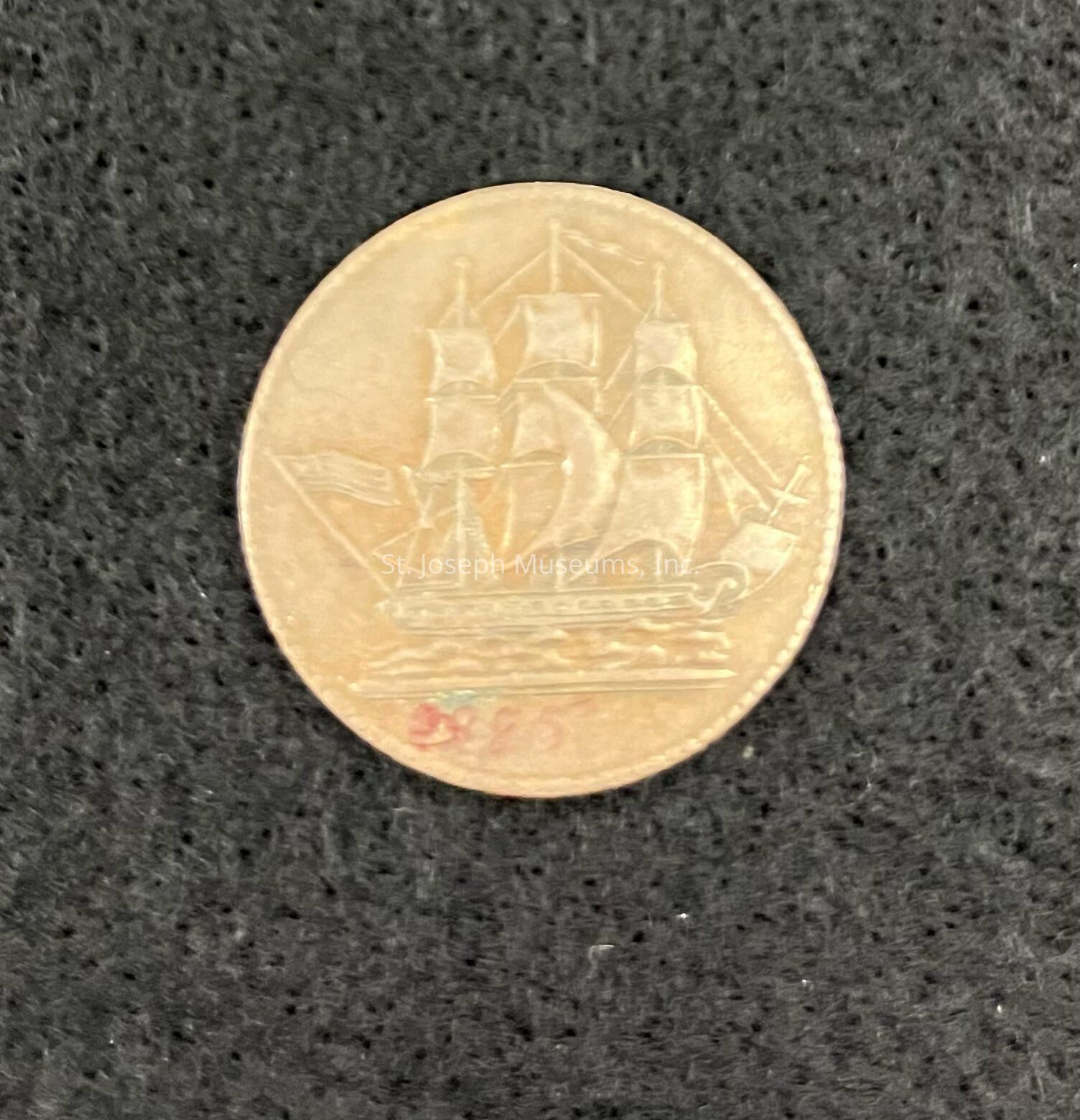 The image shows a round coin with an intricate design of a sailing ship in full sail engraved on its surface. The coin has a golden hue. The ship depicted on the coin has three prominent masts, each with sails unfurled, and it is shown in motion, symbolizing movement and exploration. Below the ship, there seems to be a small mark or series of numbers, though it is partially obscured or worn. The level of detail in the engraving is impressive, capturing the essence of a majestic ship navigating the open sea. The overall composition of the image highlights the coin's historical or cultural significance, possibly hinting at its origin from a period when maritime travel was of paramount importance. The textured surface beneath the coin adds depth to the image, allowing the viewer to focus on the coin's artwork and appreciate its craftsmanship and the story it might tell.