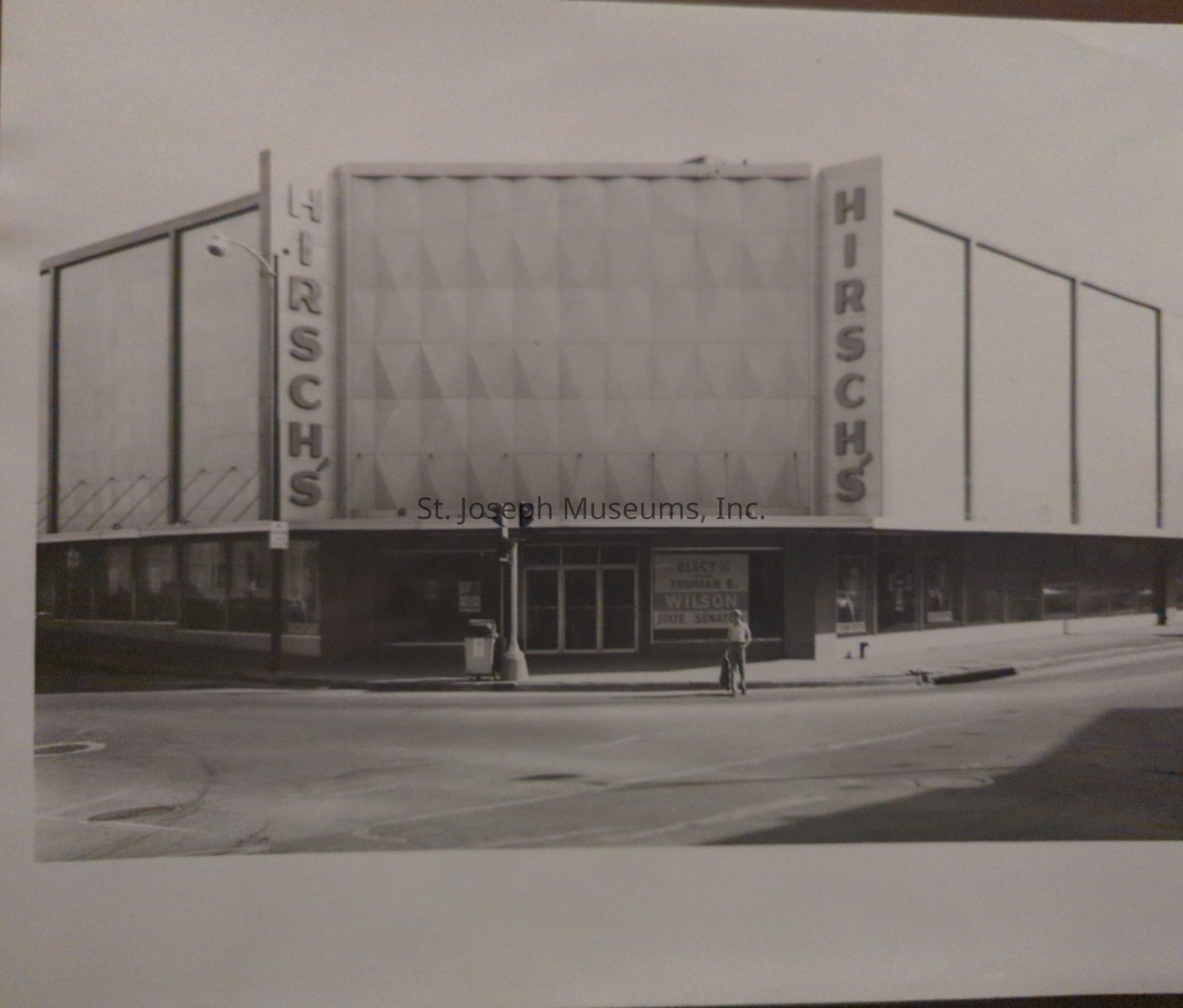 Black-and-white photograph depicting a corner building with prominent "HIRSCHS" signage, identified as Hirsch Bros. Dry Goods, situated at the intersection of 8th and Felix Street. The building has a distinct mid-century architectural style with large window displays. A person is visible on the sidewalk.