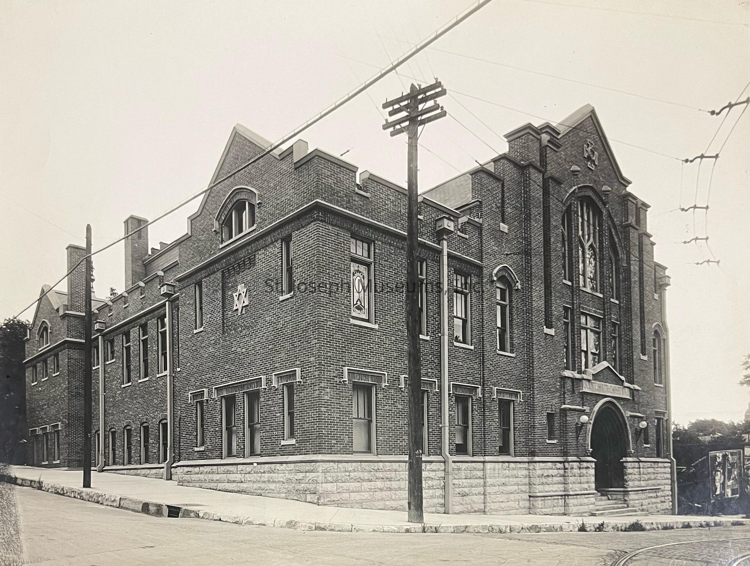 Black-and-white image depicting the historic Masonic Temple located at 6th and Robidoux in St. Joseph, Missouri, showcasing its impressive brick architecture with large arched windows, intricate stonework, and emblematic symbols that reflect its Masonic heritage, situated on a well-paved corner with telegraph poles.