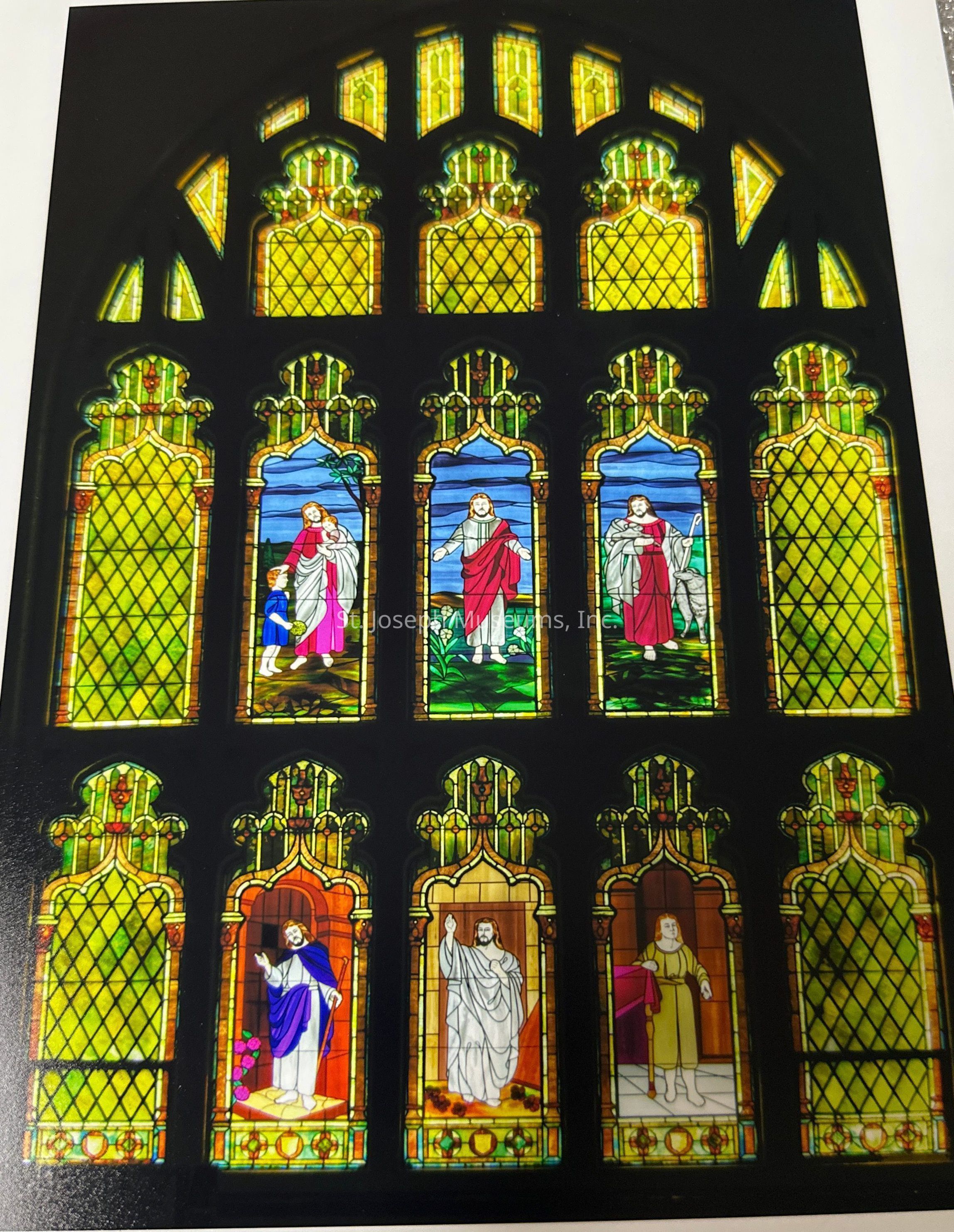 Colorized interior stained glass photo of Zion United Church of Christ window panel. There are 18 large panels with geometric decoration and a set of crosses and shields at the bottom, 6 of which have depictions of Jesus and other religious figures on them. There are an additional 12 smaller panels rounding out the arched window shape.