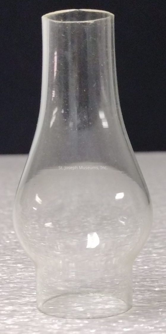 The image depicts a clear, cylindrical glass chimney with a slightly flared top and a rounded base, which is typically used as a protective cover or enclosure for lighting fixtures, such as oil lamps or candles, to shield the flame from wind while allowing the light to disperse effectively; it is placed on a light-colored textured surface, with a dark background enhancing its transparency and reflective qualities, while the minimalistic composition draws attention to the clean lines and smooth, symmetrical curves of the glass structure, emphasizing its functionality and aesthetic appeal, as well as the way it interacts with ambient light to create subtle reflections and highlights, showcasing craftsmanship in glassblowing, with the overall impression being one of elegance combined with practicality, making it a vital component in traditional and vintage illumination devices, serving both decorative and utilitarian purposes by enhancing the ambiance in various indoor and outdoor settings.