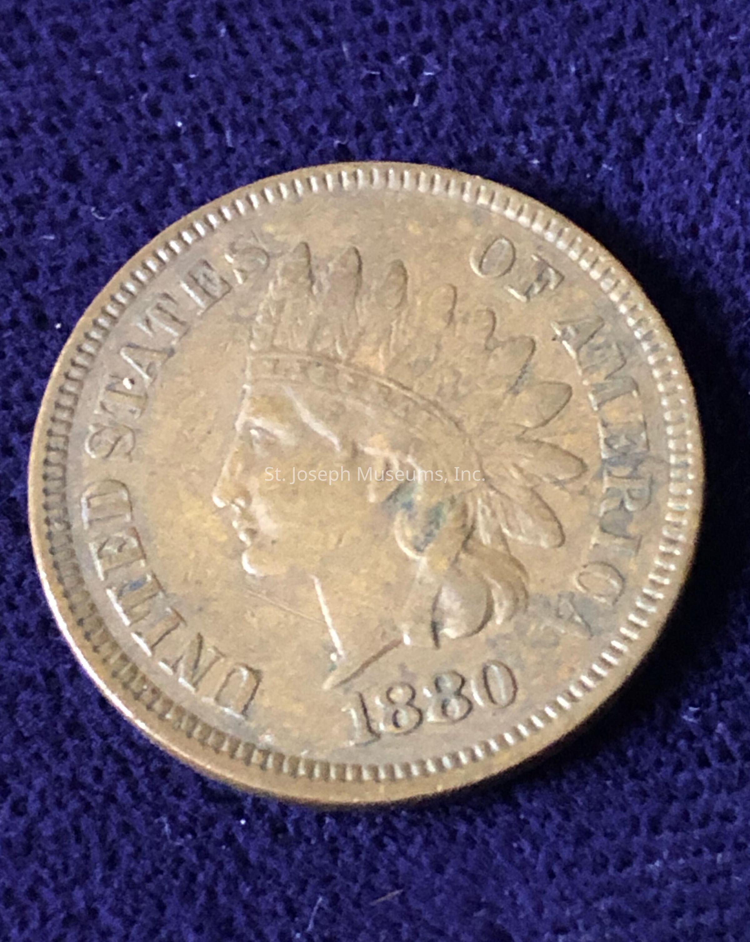 This coin is dated 1880 and features the profile of a person wearing a Native American headdress on its surface. The text encircling the profile reads "UNITED STATES OF AMERICA," clearly evident along the coin's circumference. The coin's design, detail, and patina suggest its historical significance and age, possibly attributing to its numismatic value. The intricate features of the headdress and the profile add to the overall aesthetic and historical appeal of the coin.