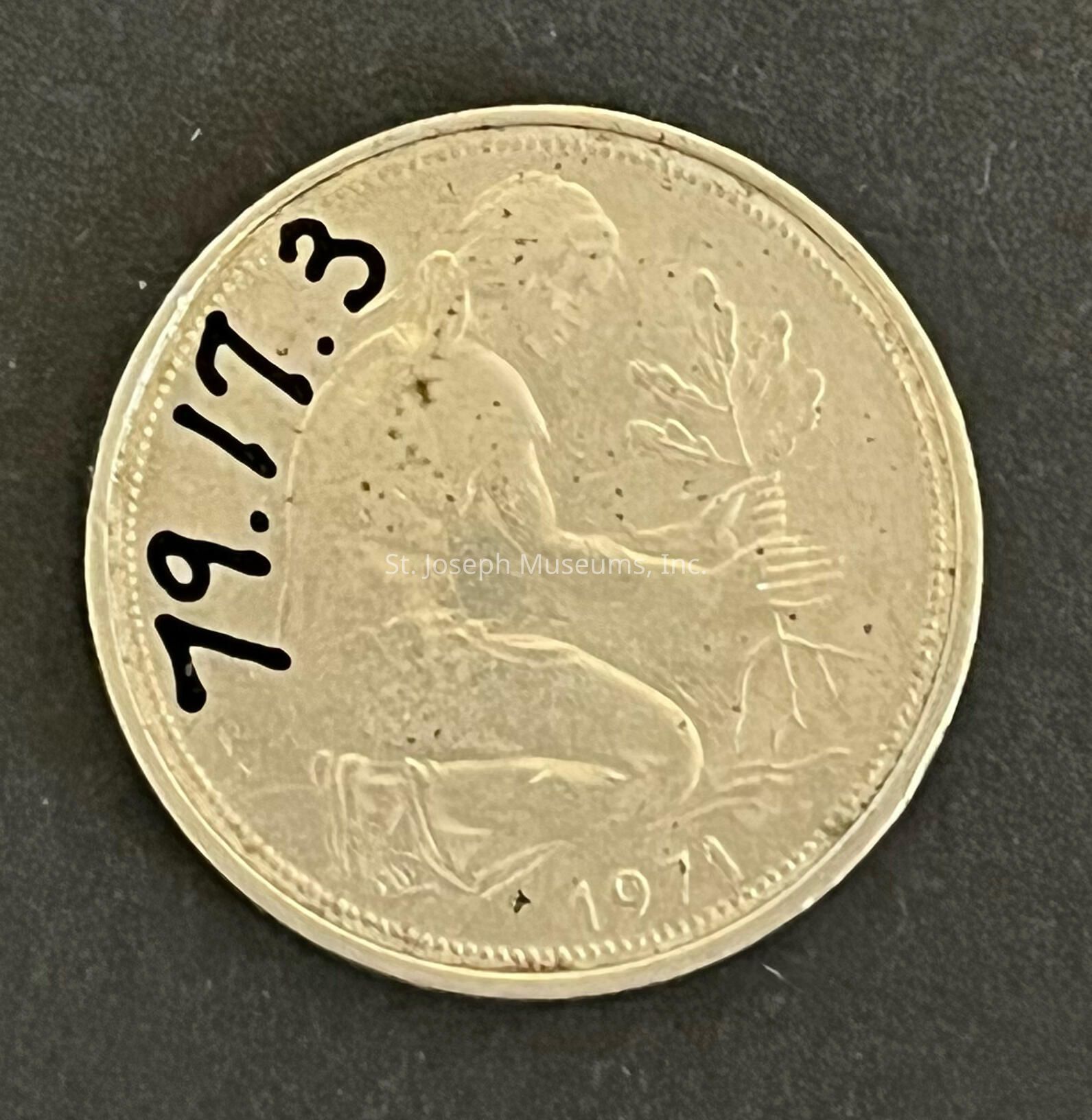 The image shows a gold-colored coin featuring a detailed engraving of a figure, possibly a woman, seated and holding a small tree or branch with leaves. Surrounding the figure is a border with raised dots. The year "1971" is printed at the bottom of the coin. To the left, the numbers "79.17.3" are marked in black ink, appearing to have been added manually. The coin sits against a dark background, allowing the intricate design and details to stand out prominently.
