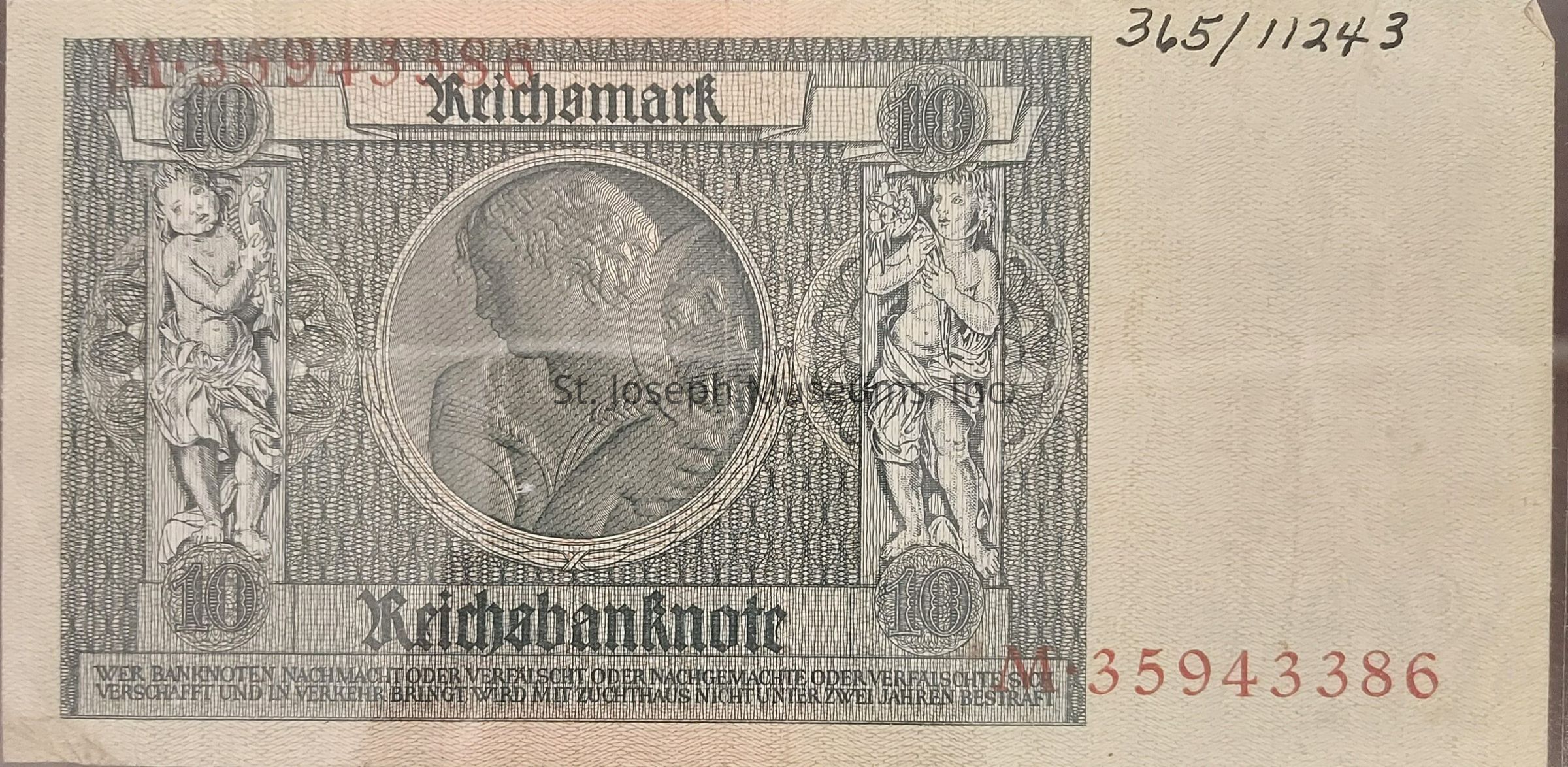 The image is of a historical banknote displaying the denomination of "10" Reichsmark, prominently positioned in each corner of the intricate design. In the center, there's a detailed engraved profile of a classical figure, surrounded by ornate patterns with two cherubic figures on either side, each holding decorative elements. The words "Reichsbanknote" are inscribed in a bold, Gothic script at the bottom, surrounded by elaborate security features typical of early 20th-century currency. Serial numbers in distinct red print appear at the top and bottom, possibly indicating its unique identification, and small printed text at the bottom warns against counterfeiting, reflecting the historical emphasis on the authenticity and security of paper currency during that era.