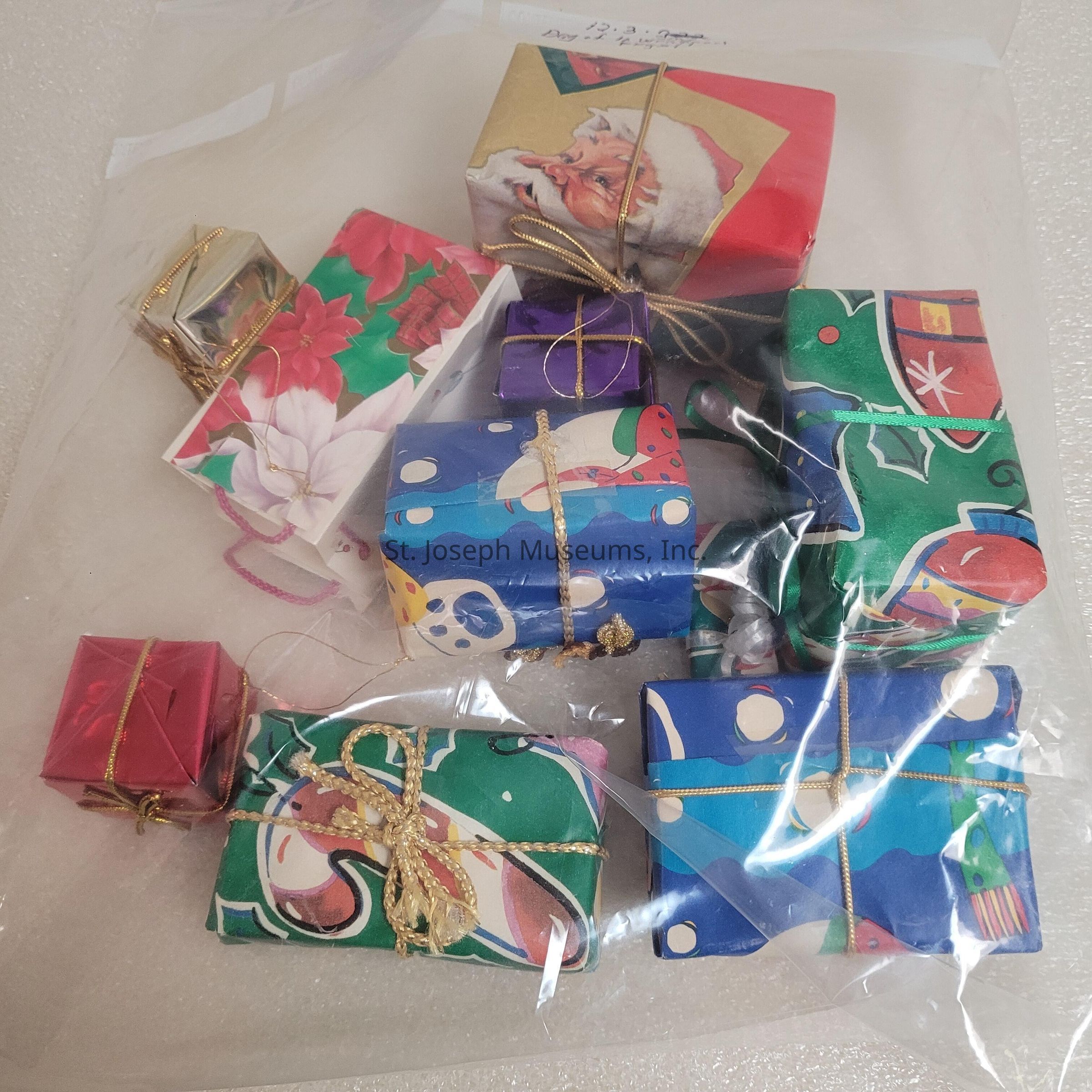 The image showcases a collection of small, intricately wrapped gifts in a clear plastic bag, each adorned with colorful and festive wrapping paper featuring vibrant holiday designs, including images of Santa Claus, poinsettias, and seasonal patterns. Several of the packages are tied with shiny, gold and pink strings, adding a touch of elegance to the assortment. The thoughtfully wrapped presents vary in size and shape, and some feature metallic hues, while others are more traditional with rich reds, greens, and blues. Each gift’s wrapping is carefully folded and secured, indicating meticulous attention to detail. The different styles and colors of the packages make for a visually engaging and festive display, suggesting a theme of celebration and generosity. The presence of such gifts hints at the joy and anticipation of the holiday season, evoking feelings of warmth, kindness, and the spirit of giving. The contents remain a mystery, piquing curiosity and adding an element of surprise, which is often associated with gift-giving traditions during holidays.