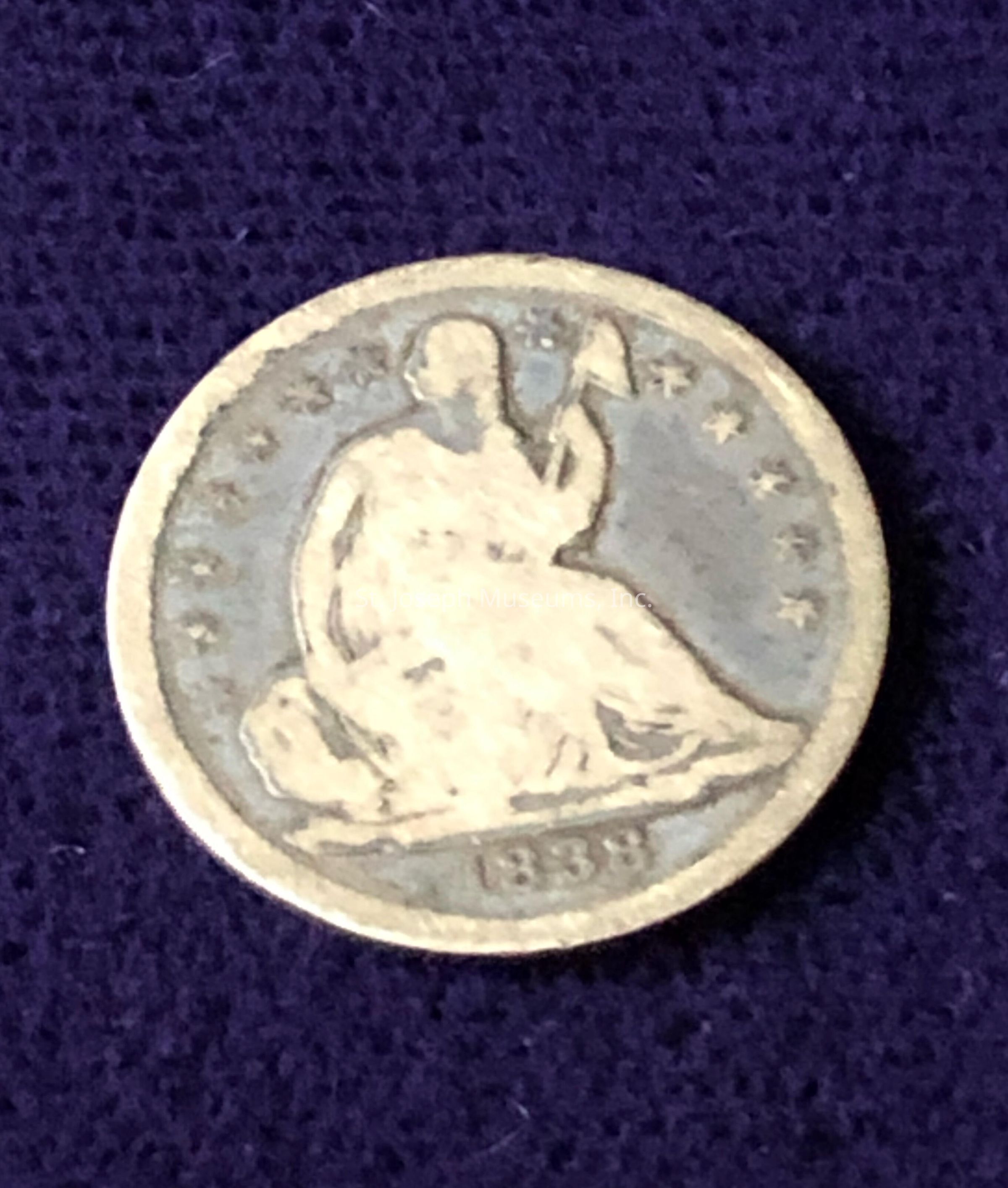 The coin features an engraving of a seated figure holding a staff, surrounded by stars along the edge, which is a classic design from historical American coinage. The date inscribed at the bottom reads "1858," suggesting it might be a Seated Liberty Dime or Quarter from that era. The intricate details of the figure and stars highlight the craftsmanship of the period. The coin's weathered appearance indicates it has been handled or aged over time, adding to its vintage appeal.