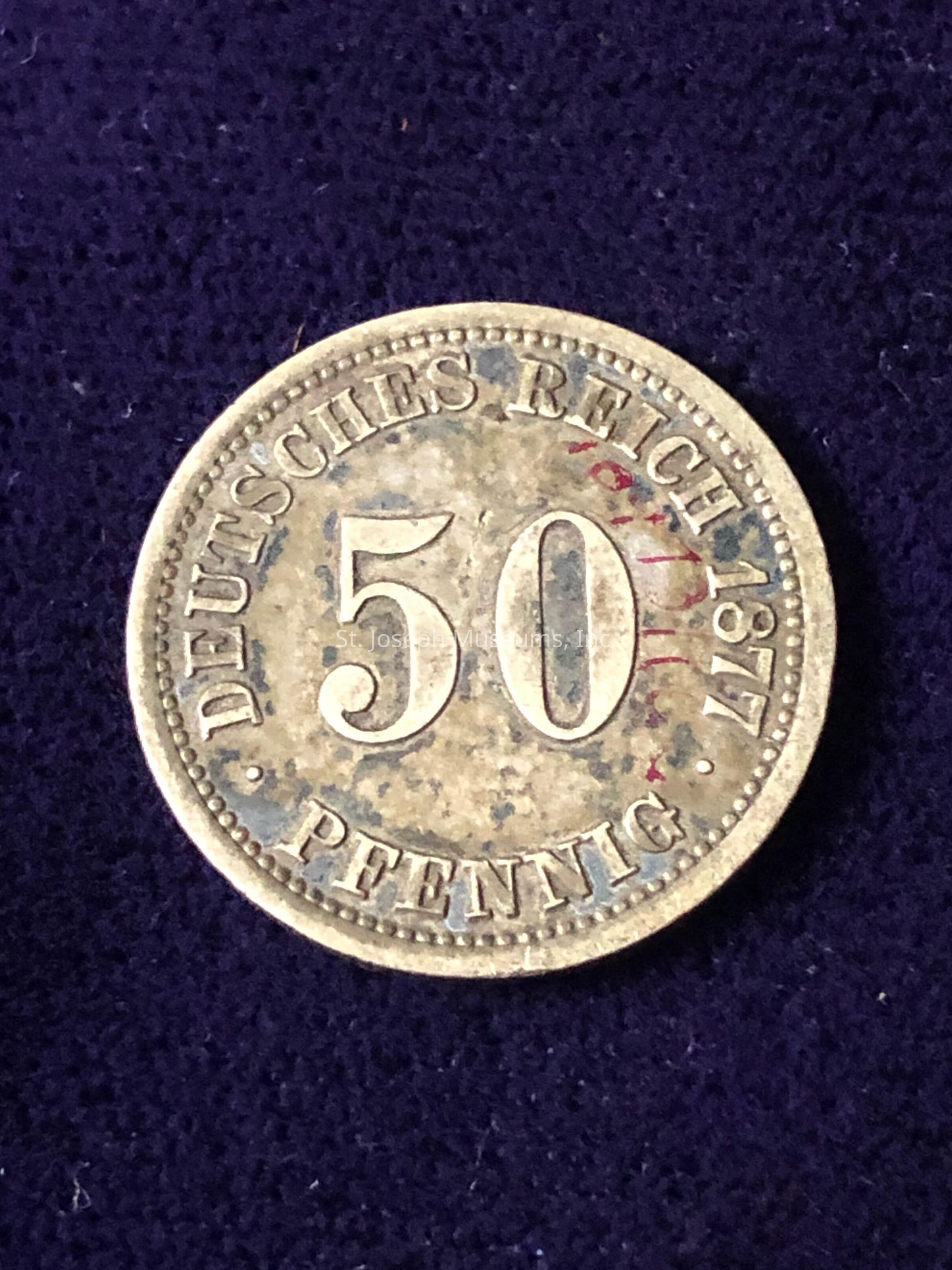 The image shows a vintage coin from the German Empire, known as the "Deutsches Reich," dated 1877, with the denomination of 50 Pfennig prominently displayed in the center. The coin has a circular design featuring intricate detailing and signs of aging, such as tarnishing and discoloration, which suggest its historical value. The word "PFENNIG" is inscribed at the bottom against a textured. The edge of the coin is detailed with small dots, adding to the overall visual appeal of this antique piece.