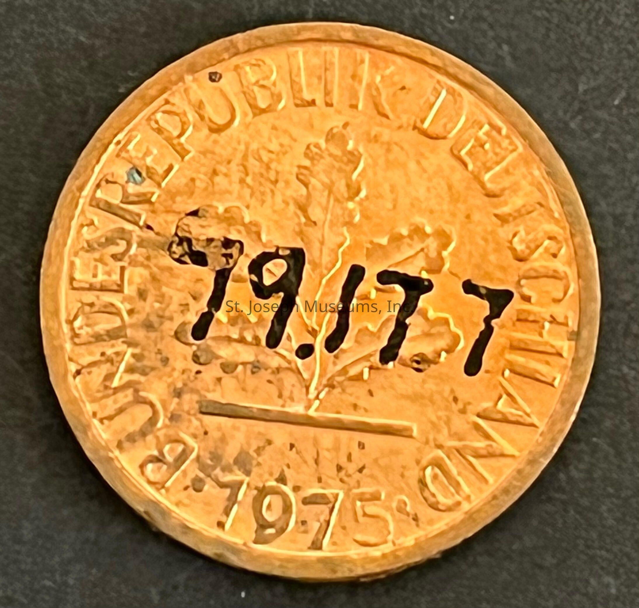 The image shows a German coin with the words "BUNDESREPUBLIK DEUTSCHLAND" inscribed around the edge, indicating its origin in Germany. At the bottom, the year "1975" is engraved, signifying its minting date. In the center, there is an embossed design of an oak leaf, a common motif on German currency, symbolizing strength and endurance. Furthermore, the numbers "19.177" are written prominently across the coin in black ink, which appears to be an addition rather than part of the original minting. The coin has a golden hue, suggesting it is made of a brass-like material. The overall appearance of the coin, along with its engraved details and additional markings, gives it a distinctive and historical character. The visible texture and slight discoloration on the coin's surface suggest it has aged over time, adding to its uniqueness. The coin is positioned against a dark background, accentuating its details and enhancing its visibility.